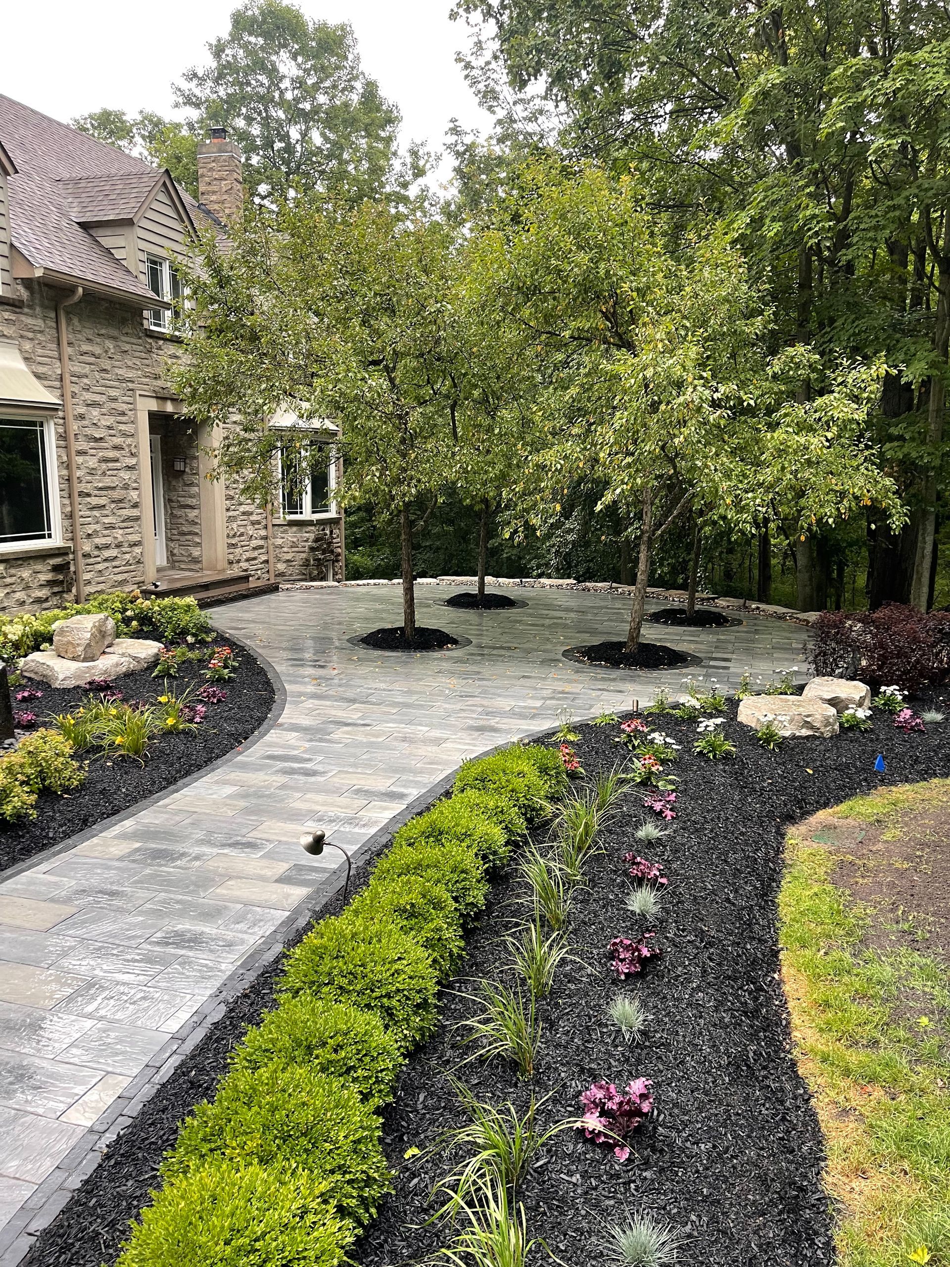 A stone house with a walkway leading to it surrounded by trees and bushes.