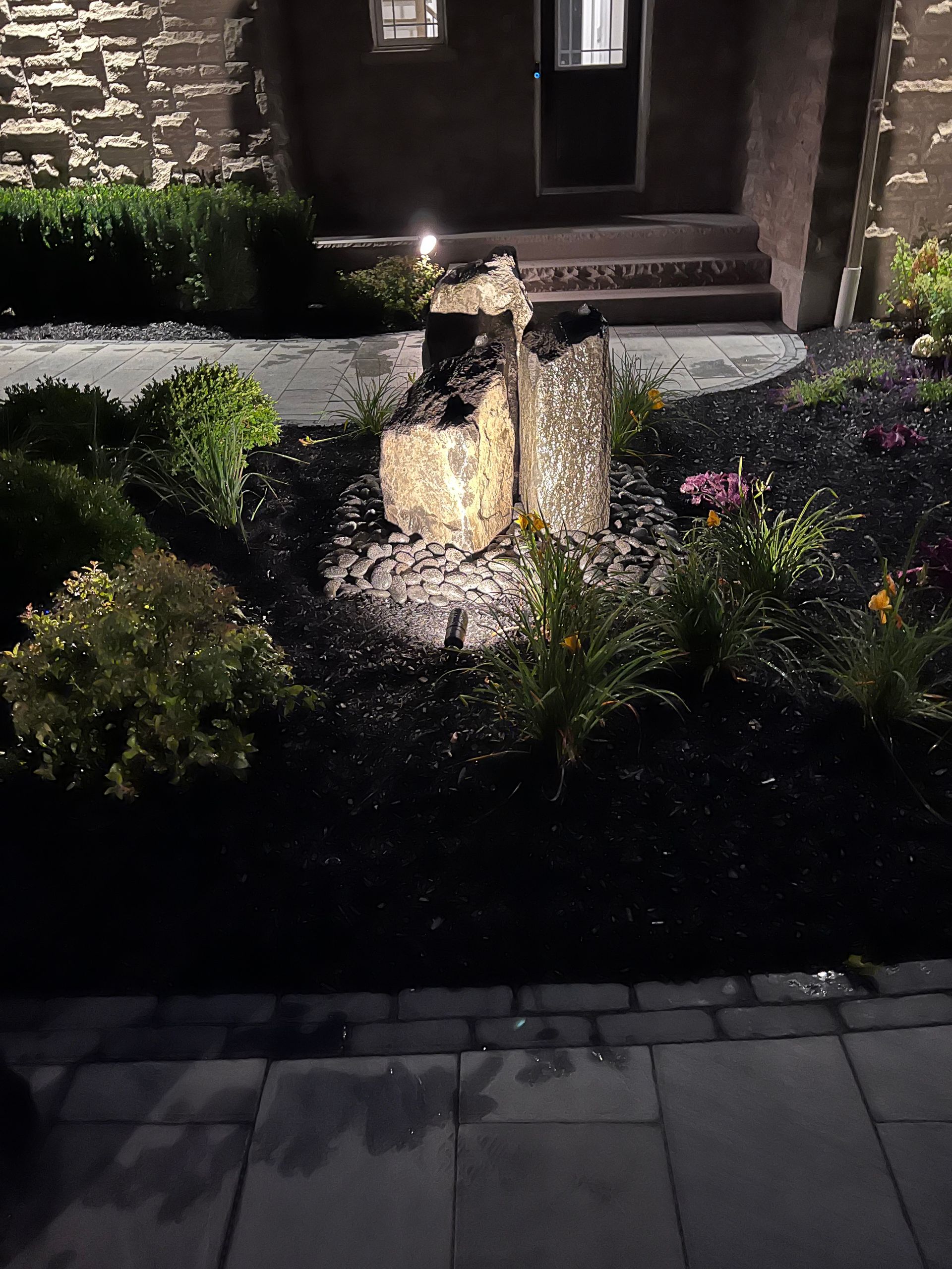 A fountain in a garden in front of a house at night.