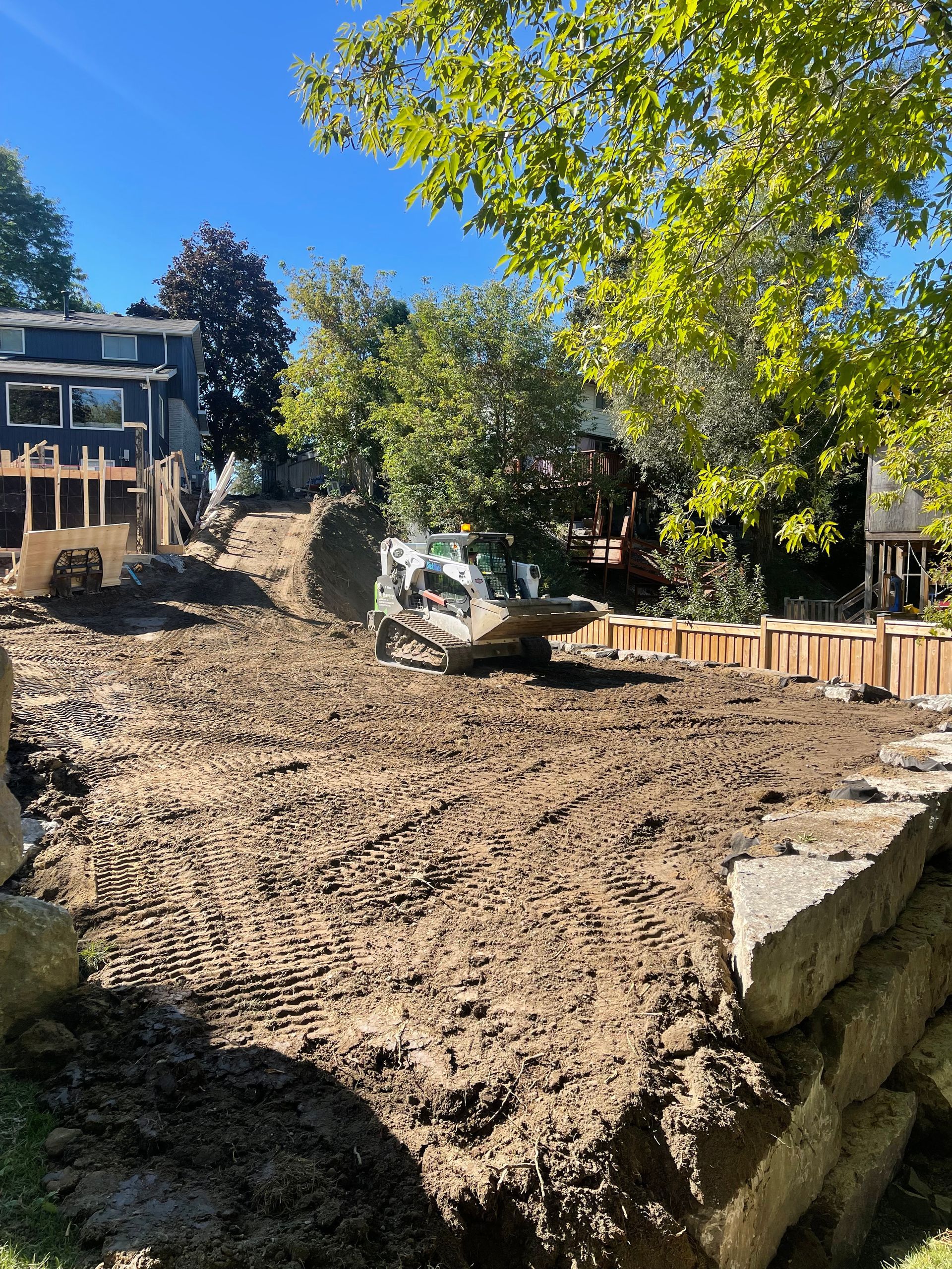 A construction site with a house in the background and a bulldozer in the foreground.