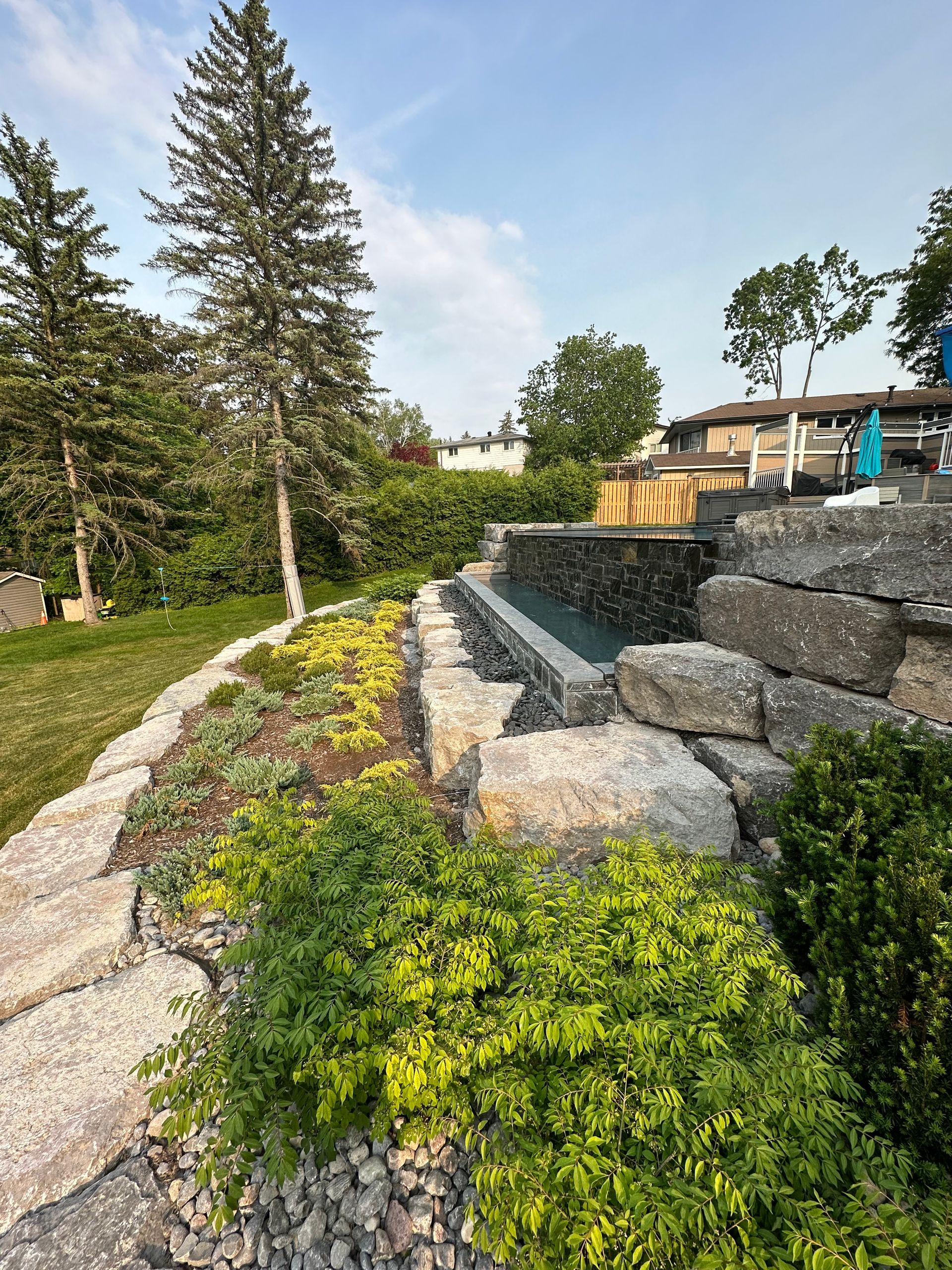 A large rock wall surrounds a swimming pool in a backyard.