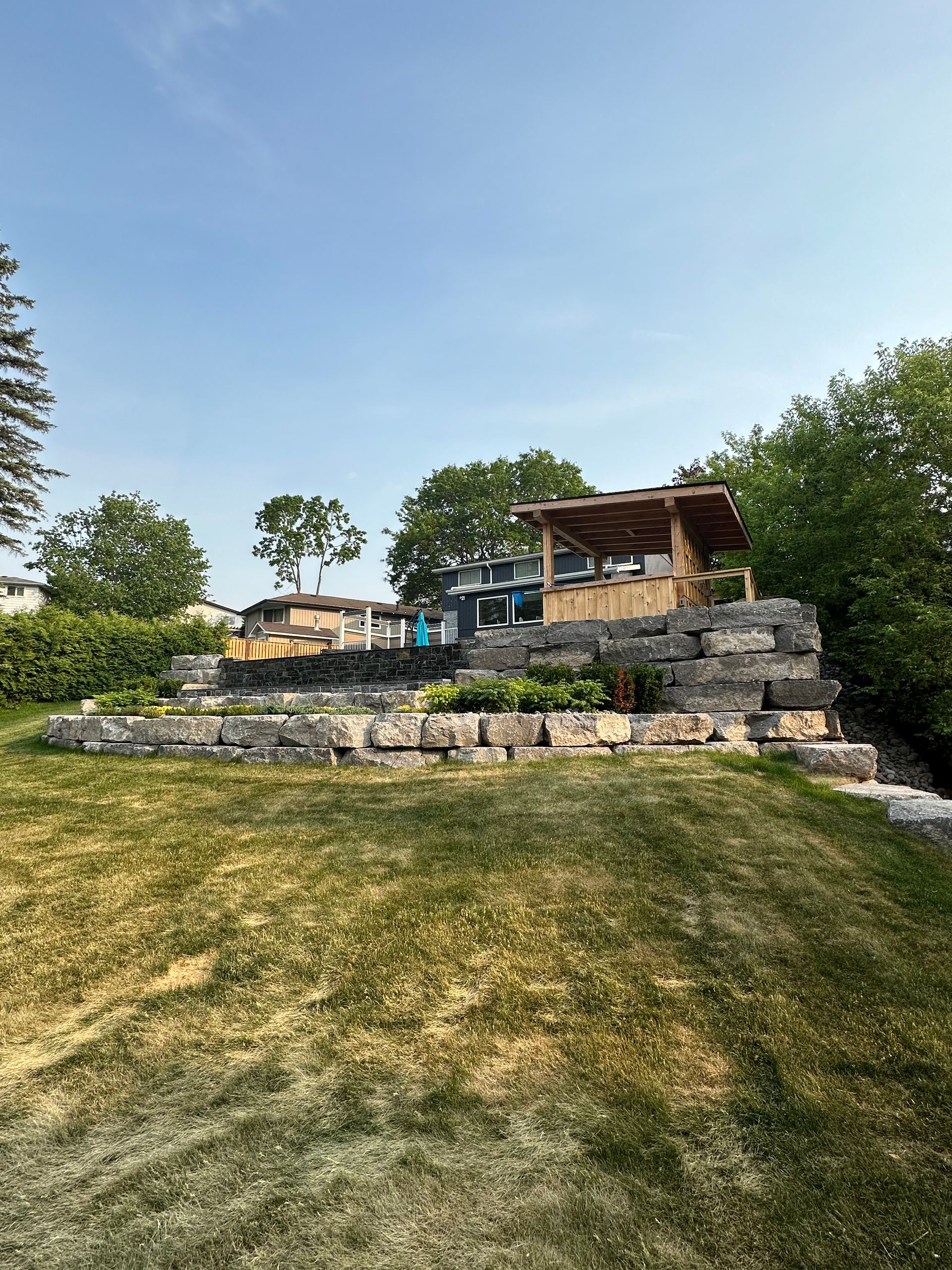A large lawn with a stone wall and a house in the background.
