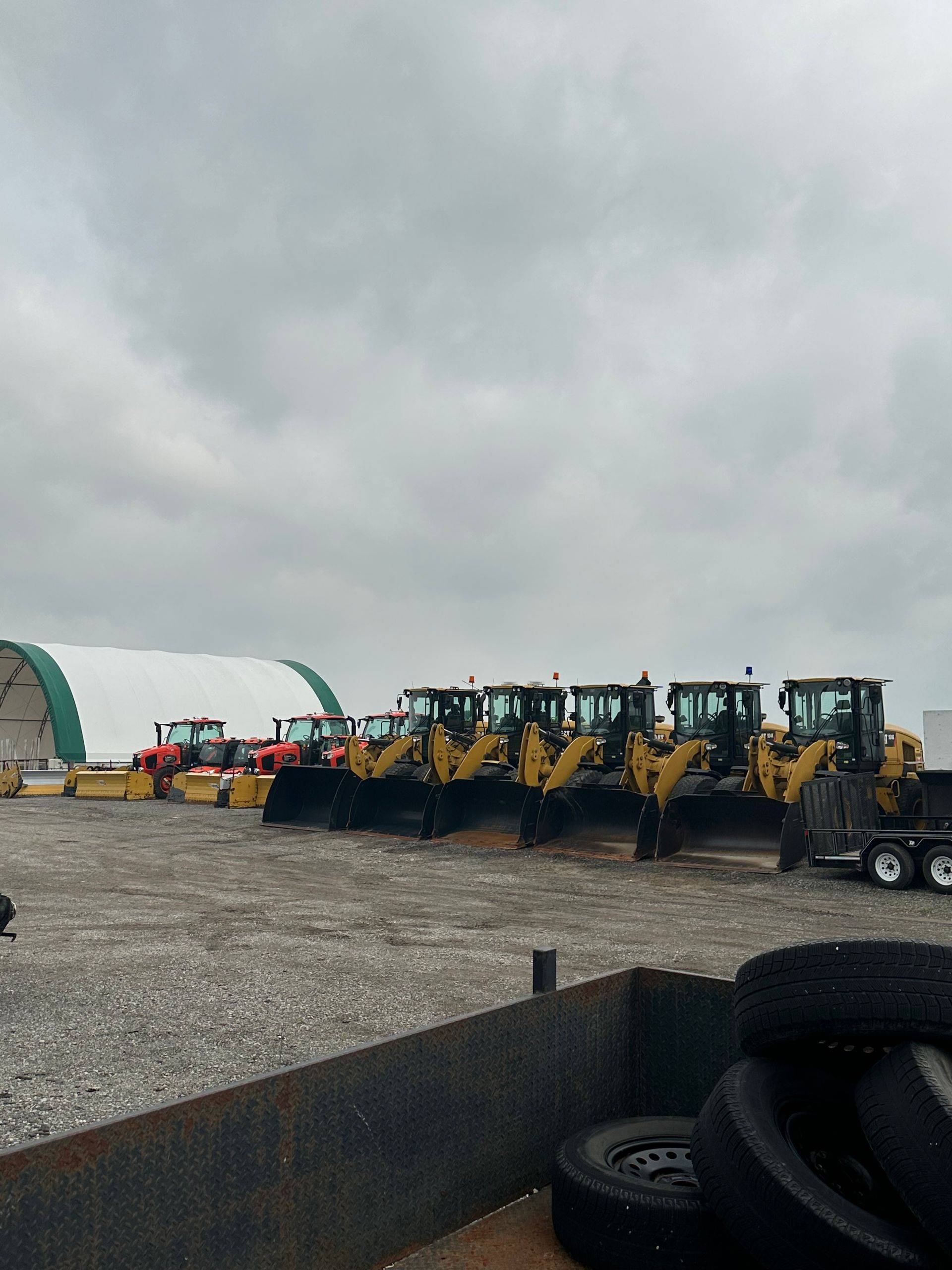 A row of bulldozers are parked in a gravel lot.