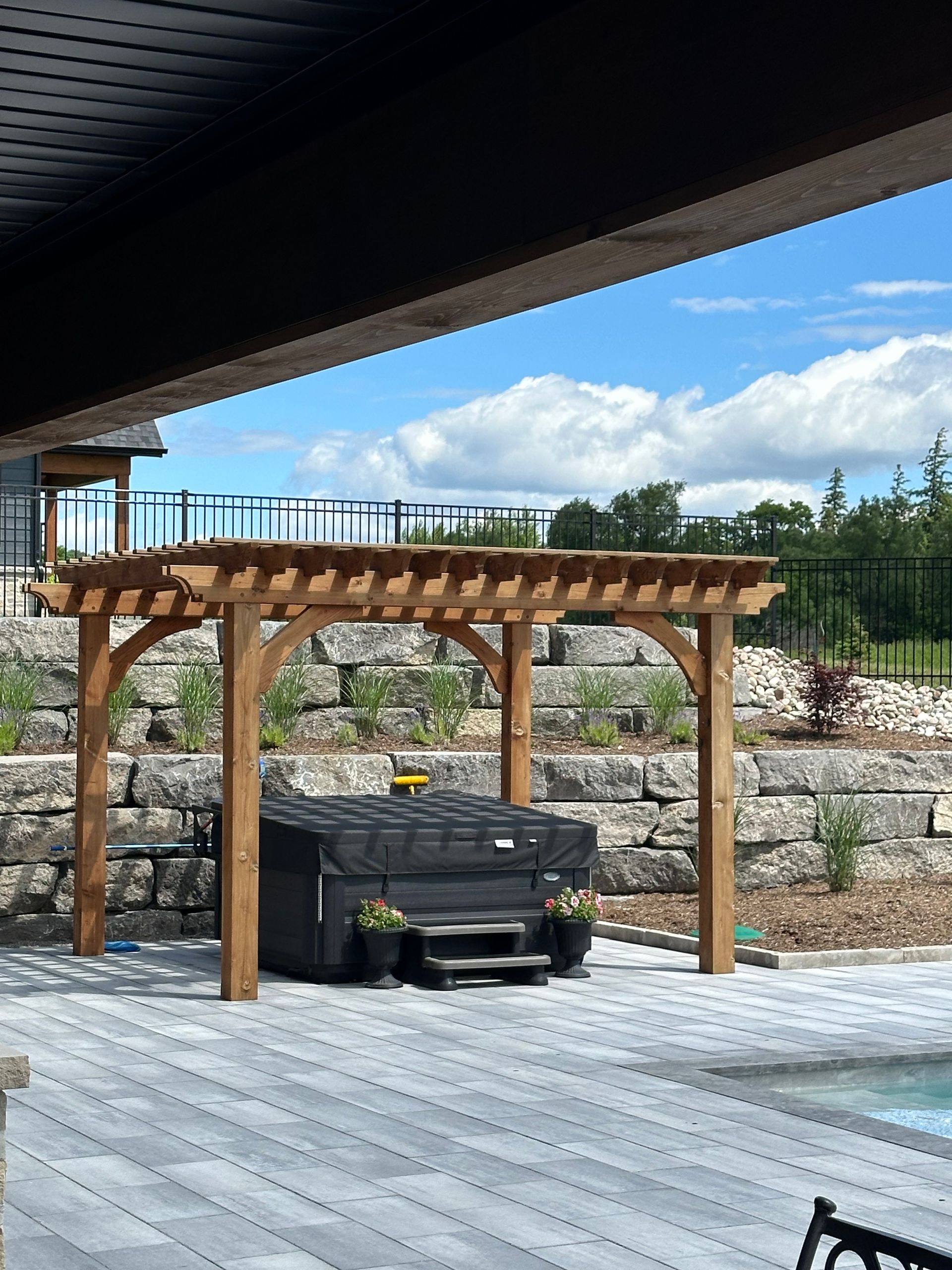 A hot tub is under a wooden pergola next to a pool.