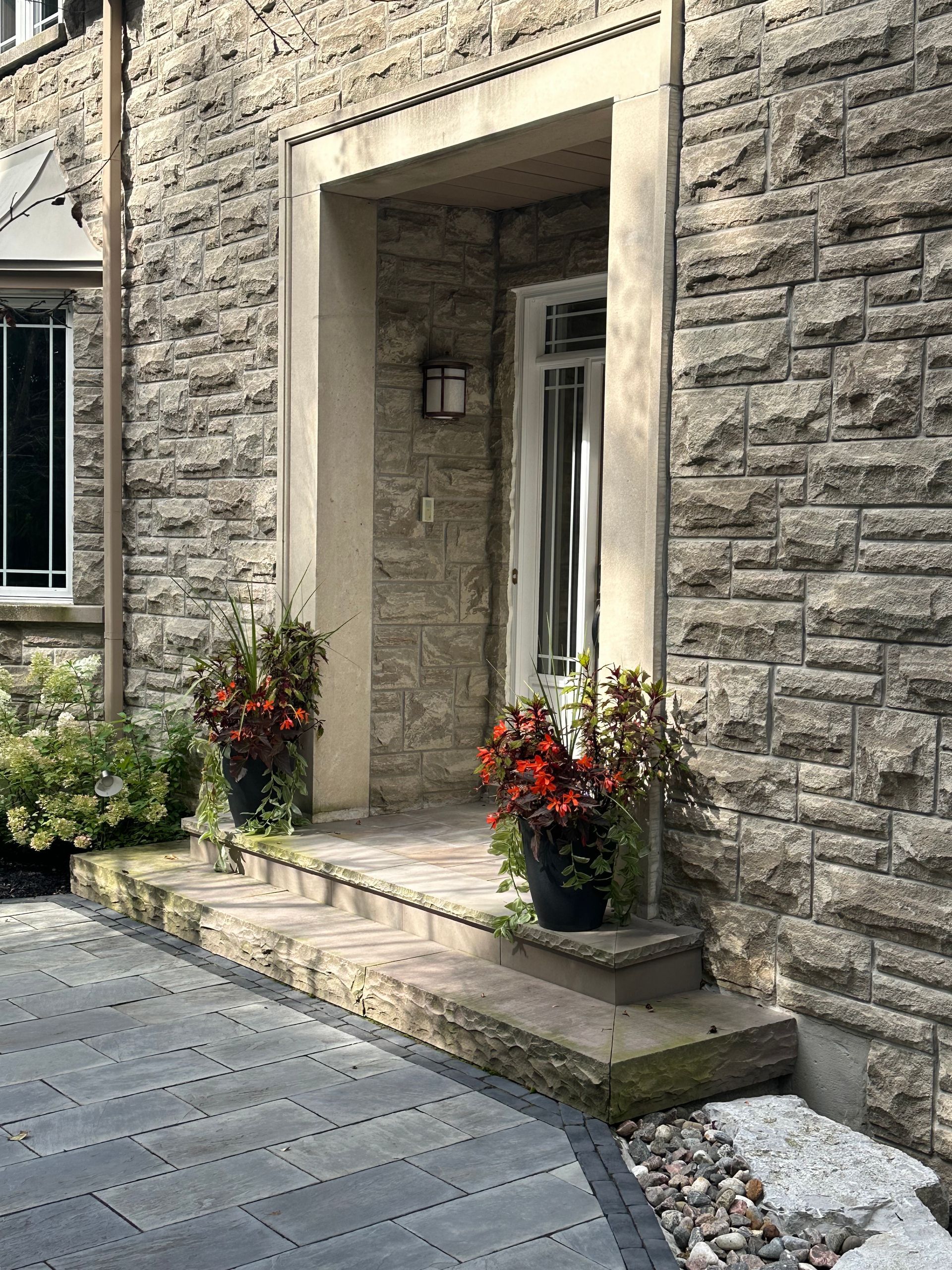 The front door of a brick house with flowers in pots on the porch.