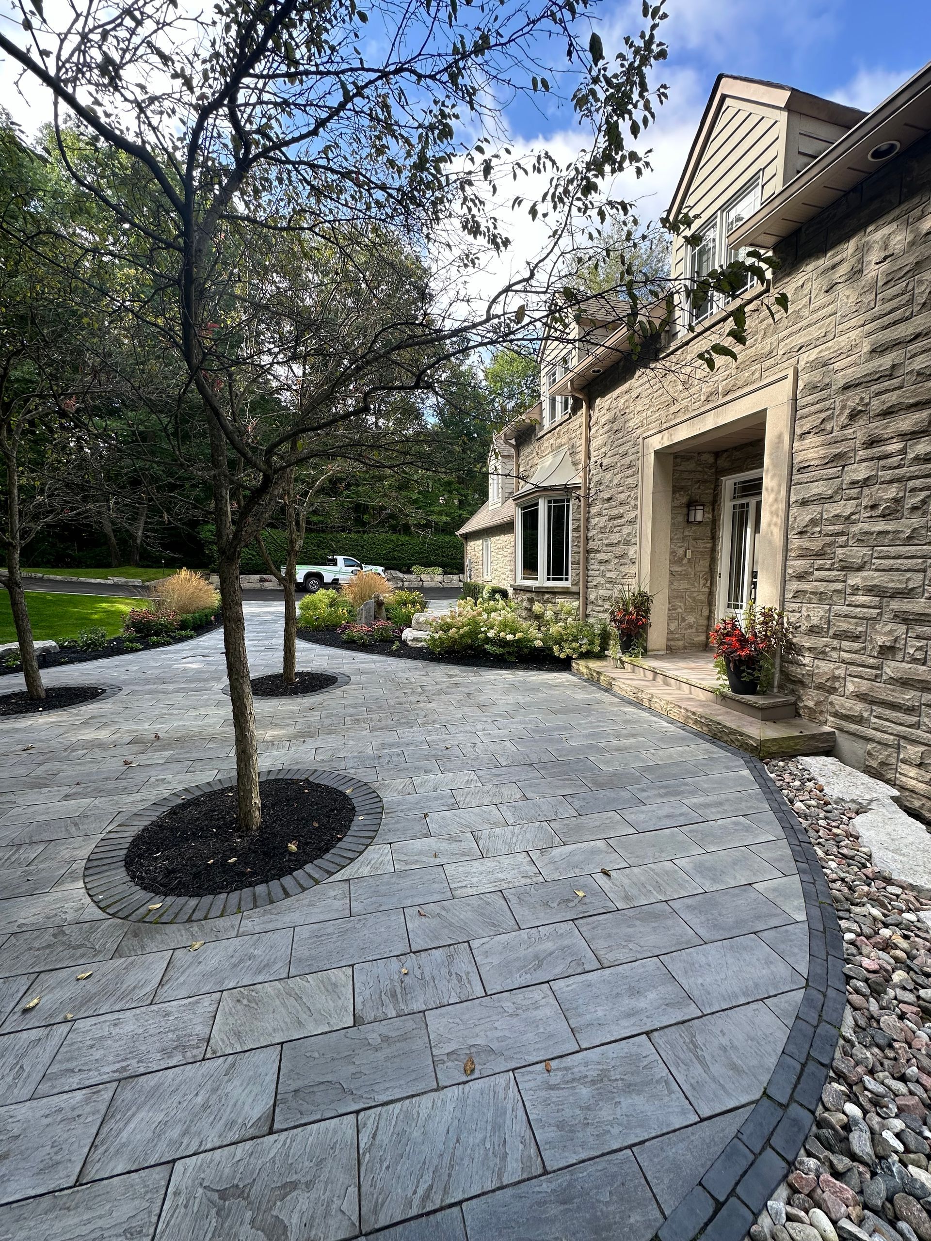 A stone house with a circular driveway and trees in front of it.