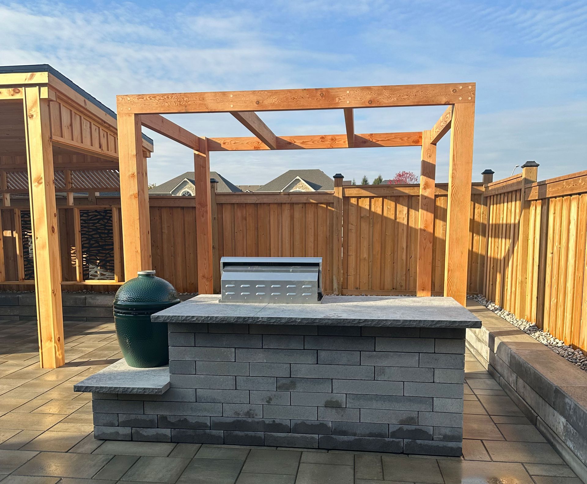 A large green egg is sitting on top of a brick counter under a wooden pergola.