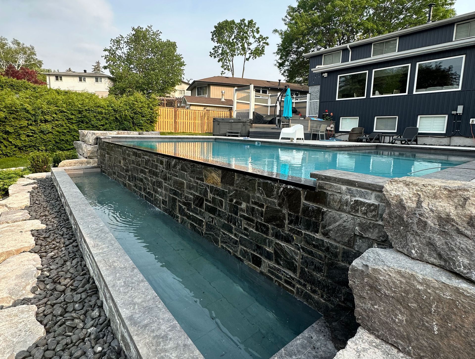 A large swimming pool is surrounded by a stone wall and a house in the background.