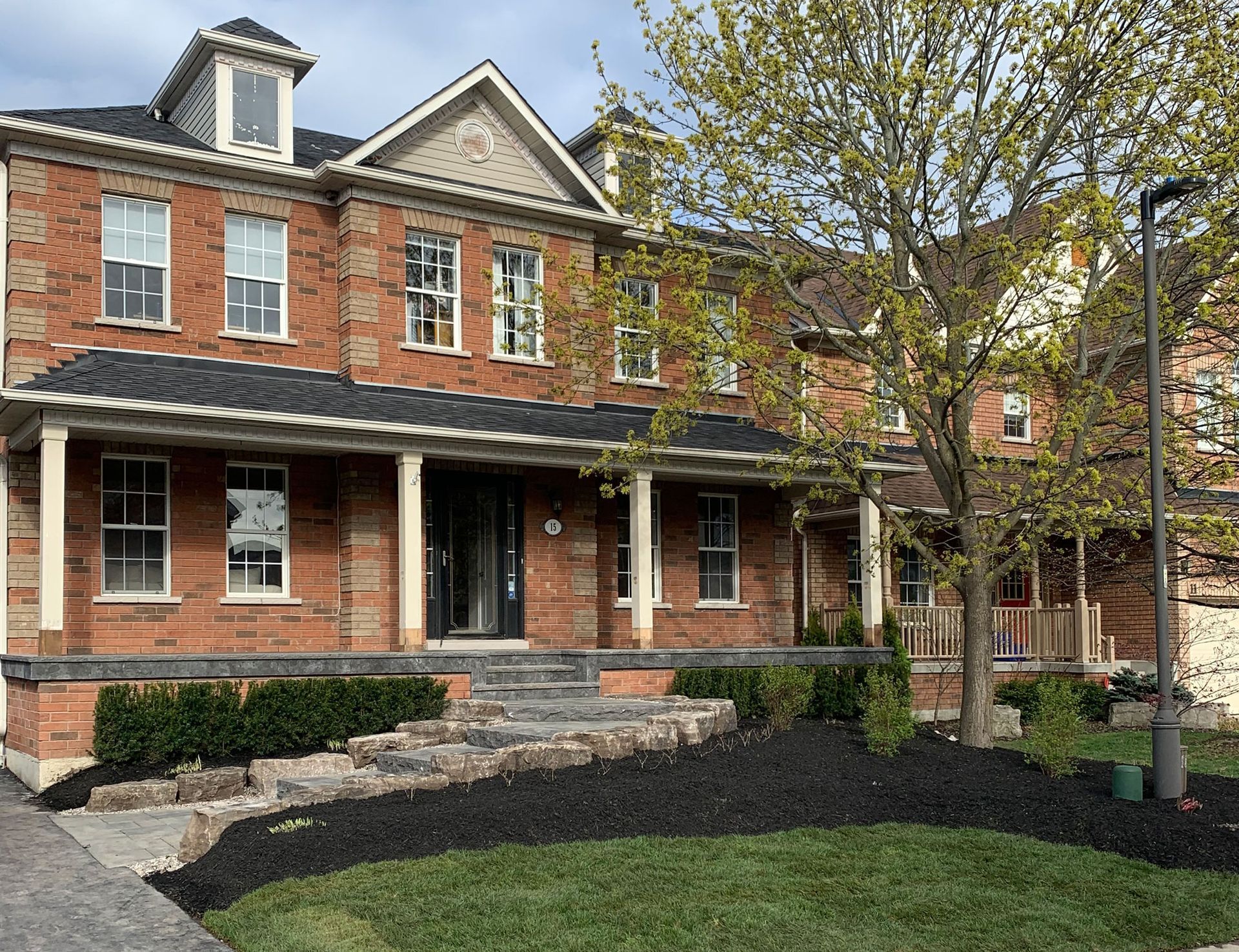 A large brick house with a large porch and a tree in front of it.