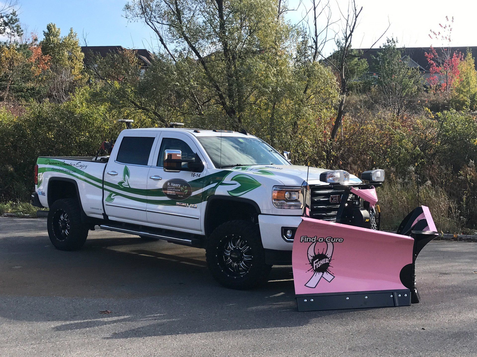 A white truck with a pink snow plow on the front is parked on the side of the road.