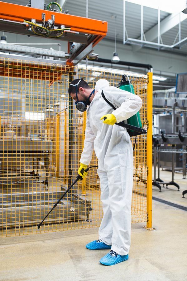 A Man In A Protective Suit Is Spraying A Machine In A Factory — Cantips Pest Control in Albury, NSW
