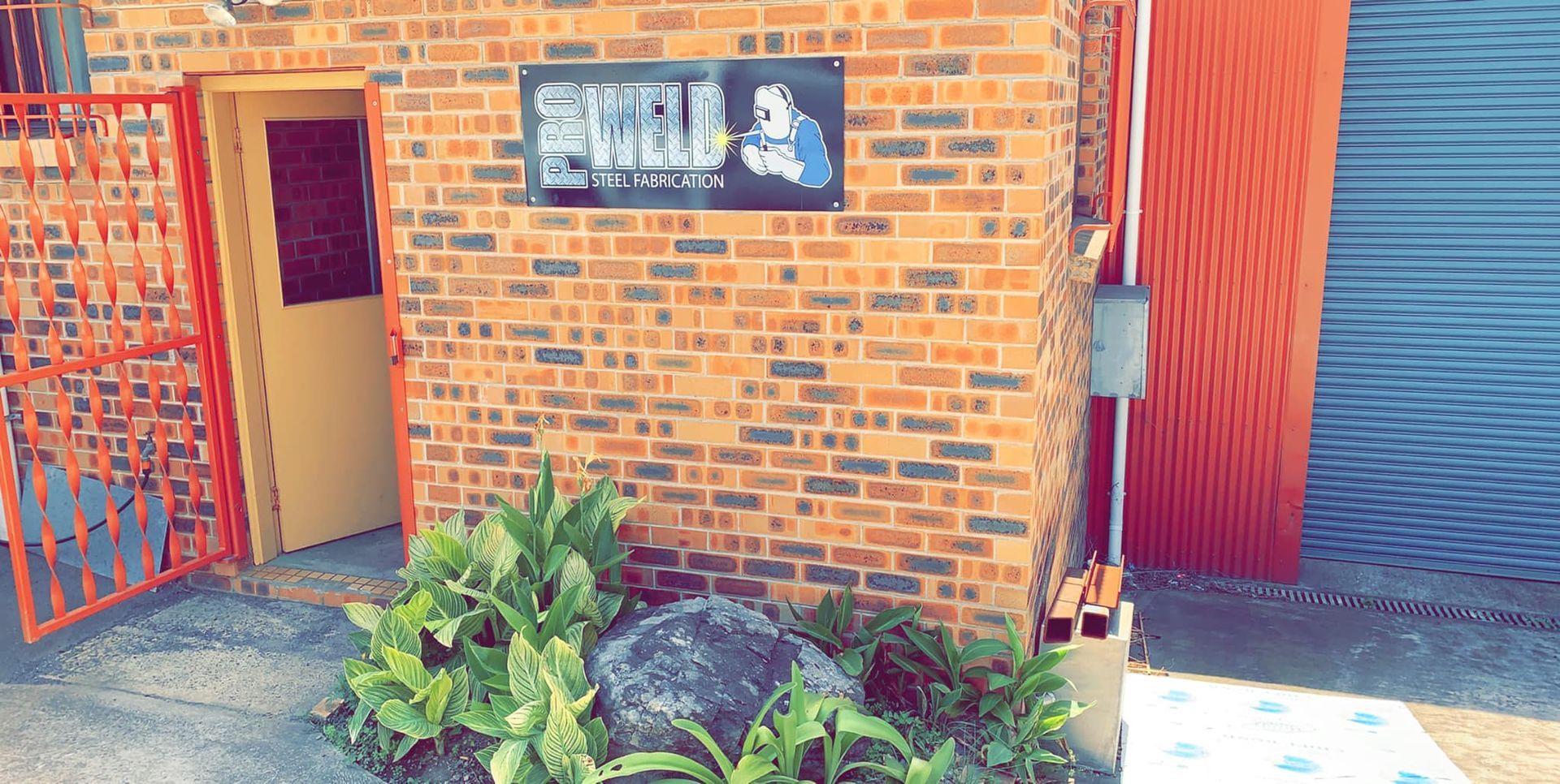 A Brick Building With a Sign on the Side of It and a Red Door — Proweld Steel Fabrication In Unanderra, NSW