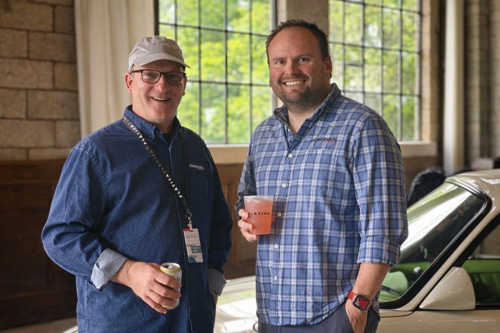 Two men smiling and holding drinks beside a car in a covered outdoor area | Eurotech Knoxville