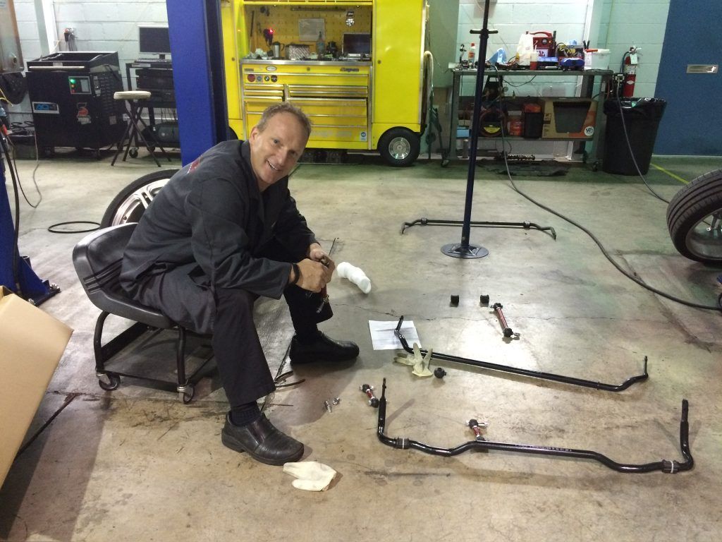 Mechanic crouches in a garage beside two metal frames on the floor, with tools and equipment in the background. | Eurotech Knoxville