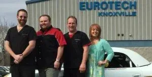 Four people standing outside Eurotech Knoxville beside a white car, smiling.
