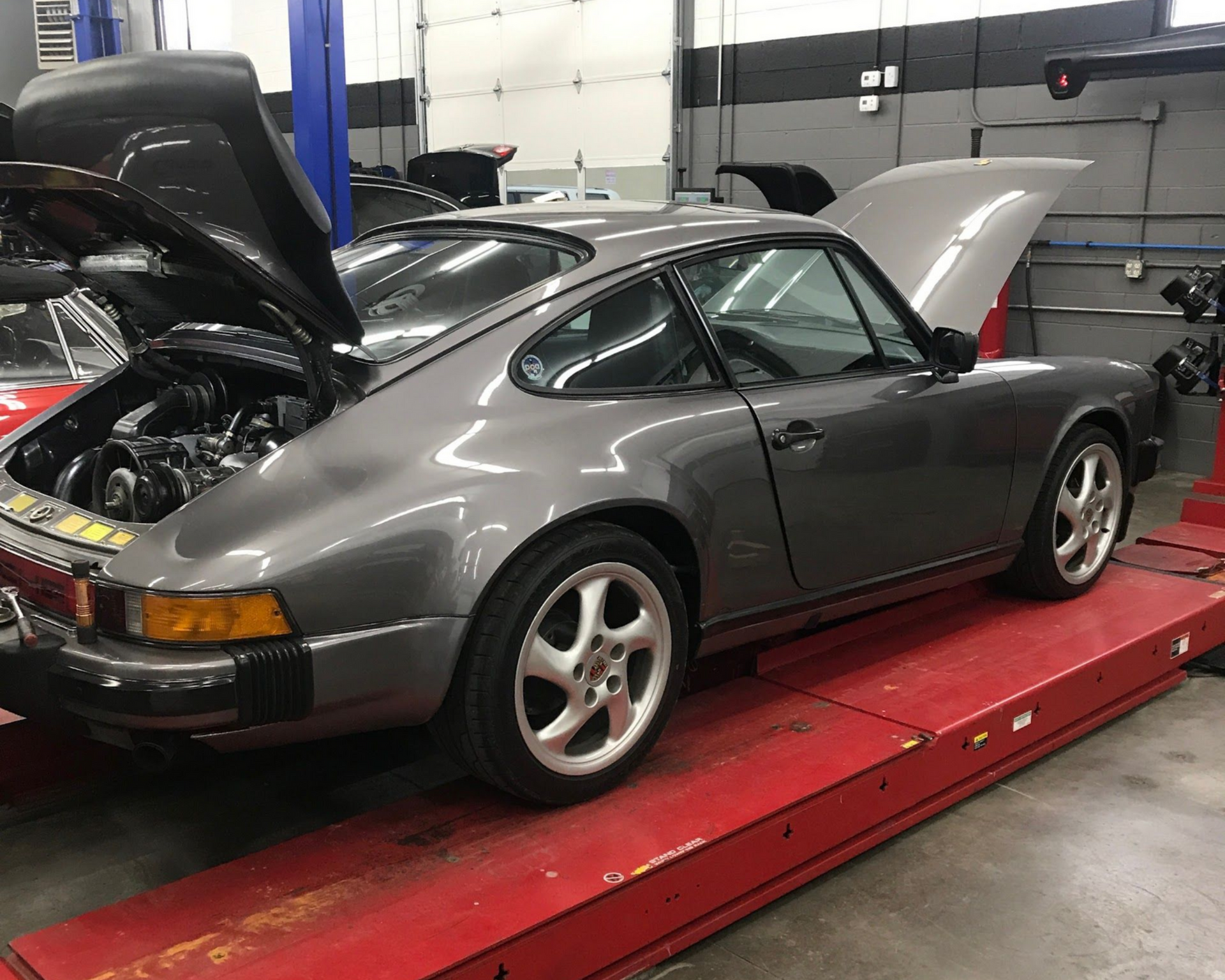 Gray Porsche 911 on a red lift in a garage, with front and rear hoods open. | Eurotech Knoxville