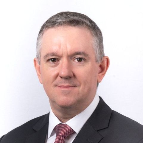 Portrait of a man in a dark suit, white shirt, and red tie against a white background