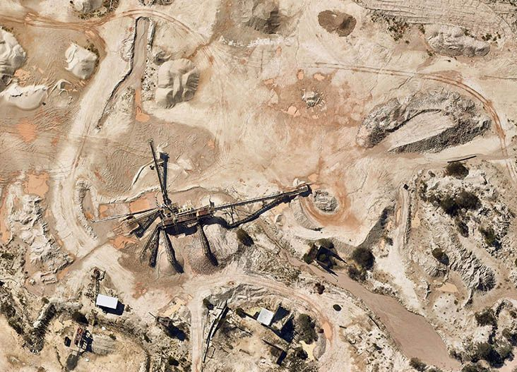 Overhead view of a construction site with a large excavator in sandy, rocky terrain