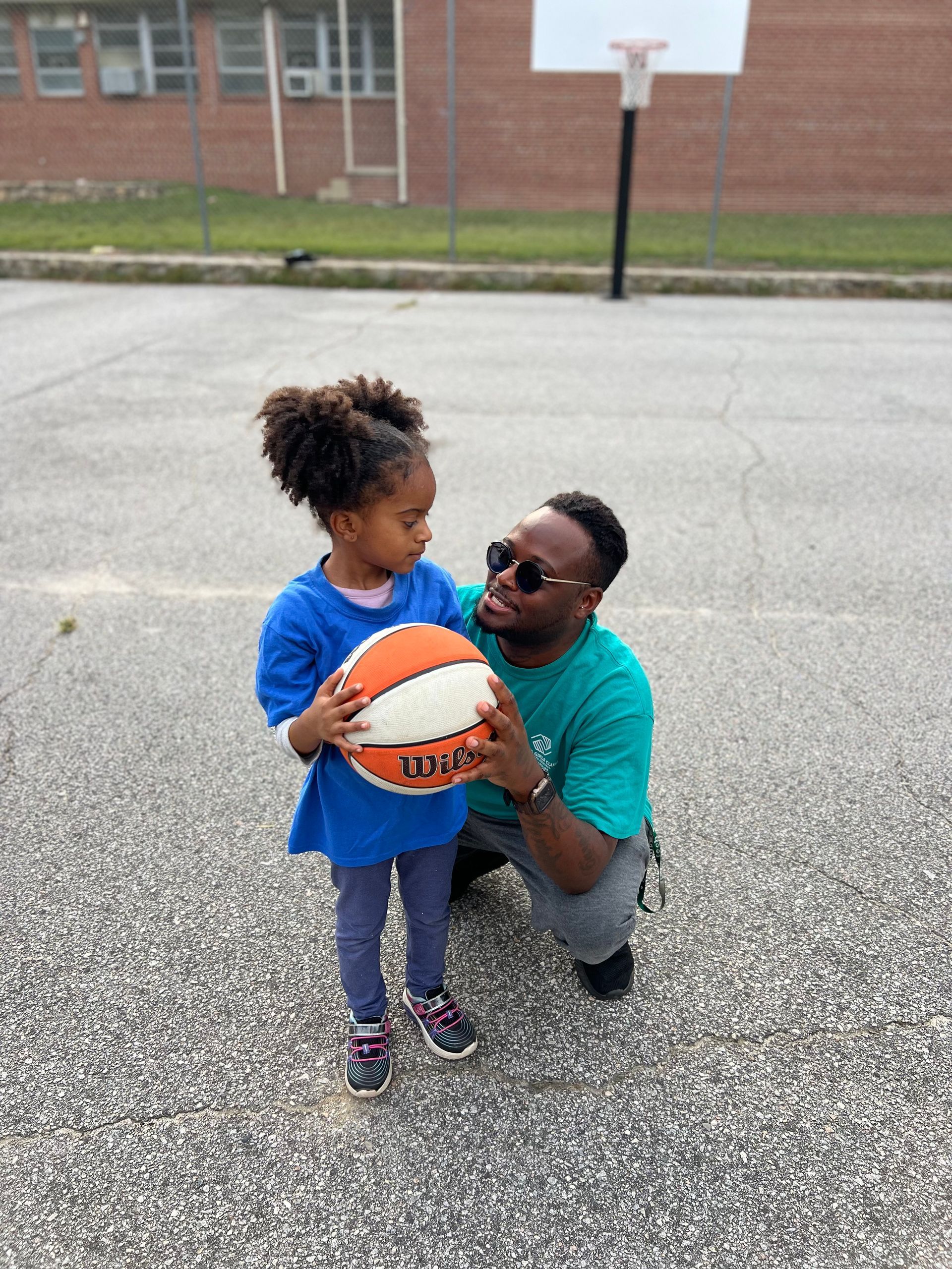 A man is kneeling down next to a little girl holding a spalding basketball