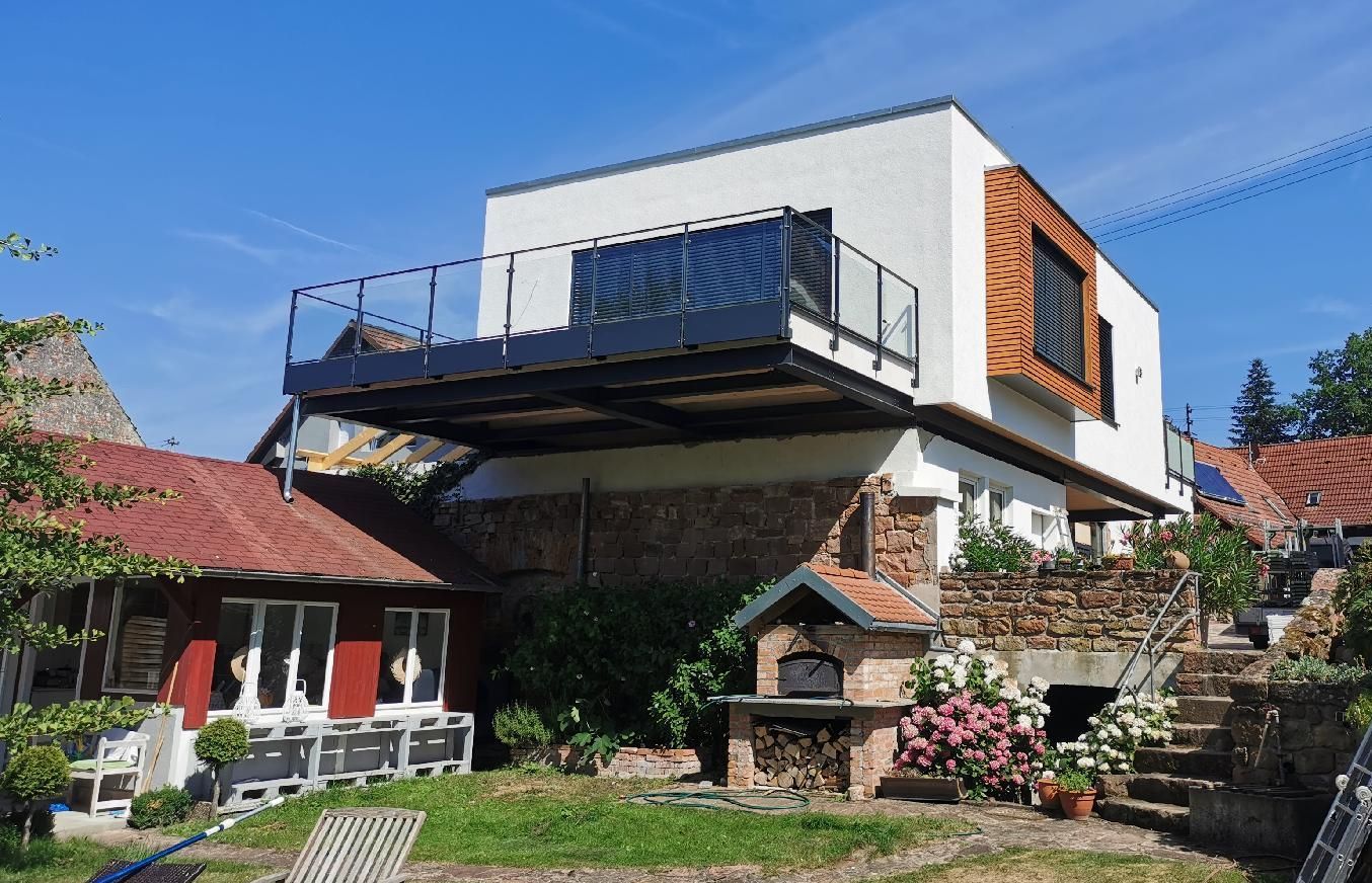 Ein modernes Einfamilienhaus vom Garten aus fotografiert. Der große Balkon ragt über einen Teil des Gartens