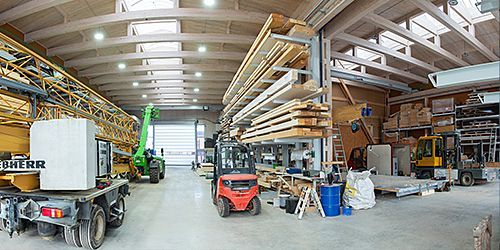 Ein Foto des Inneren der neuen Fertigungshalle. Es sind Stapler und Kräne sowie gelagertes Holz zu sehen