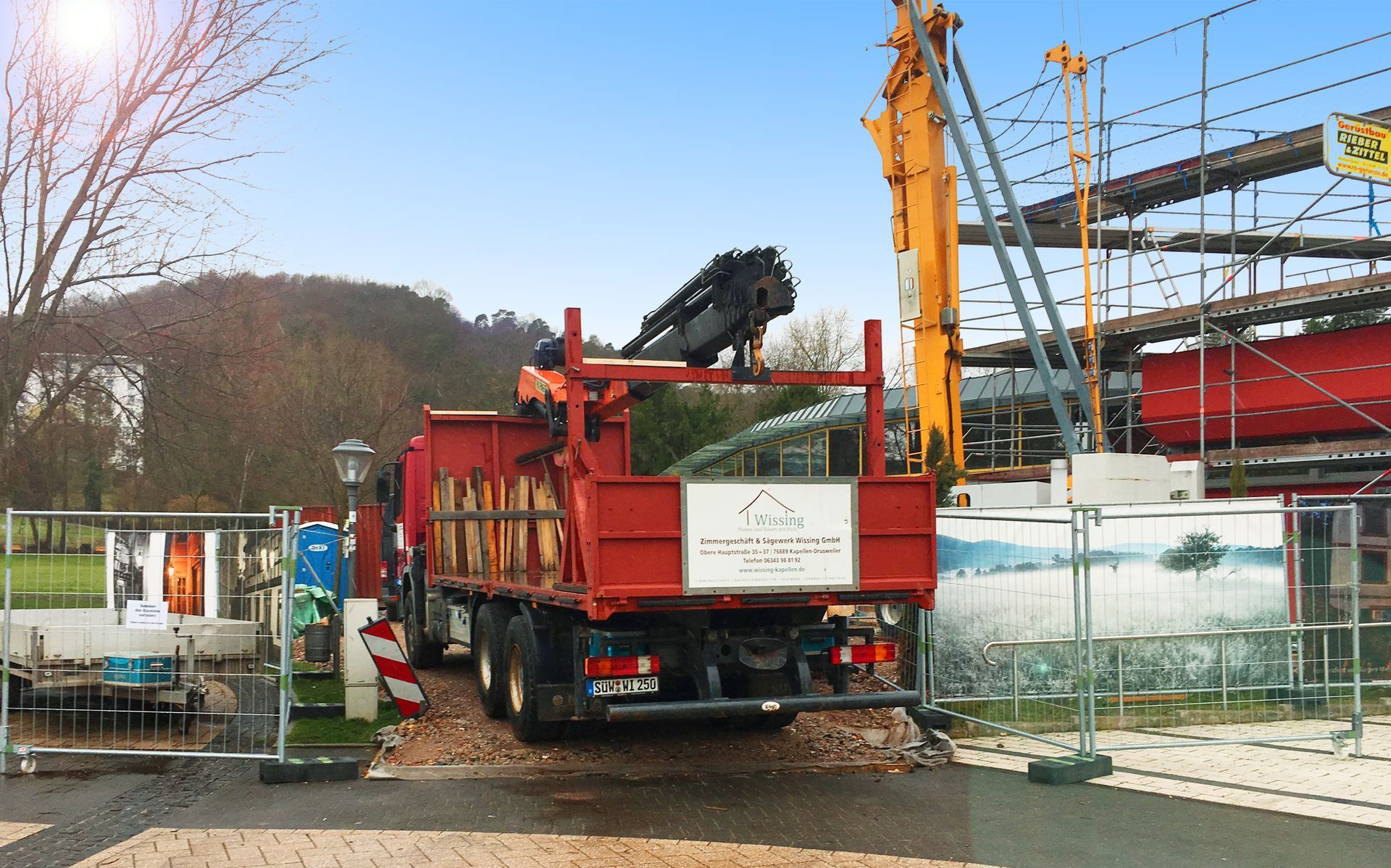 Eine eingerichtete Baustelle mit Bauzäunen, rechts ist ein Gerüst zu sehen und in der Mitte steht ein roter LKW