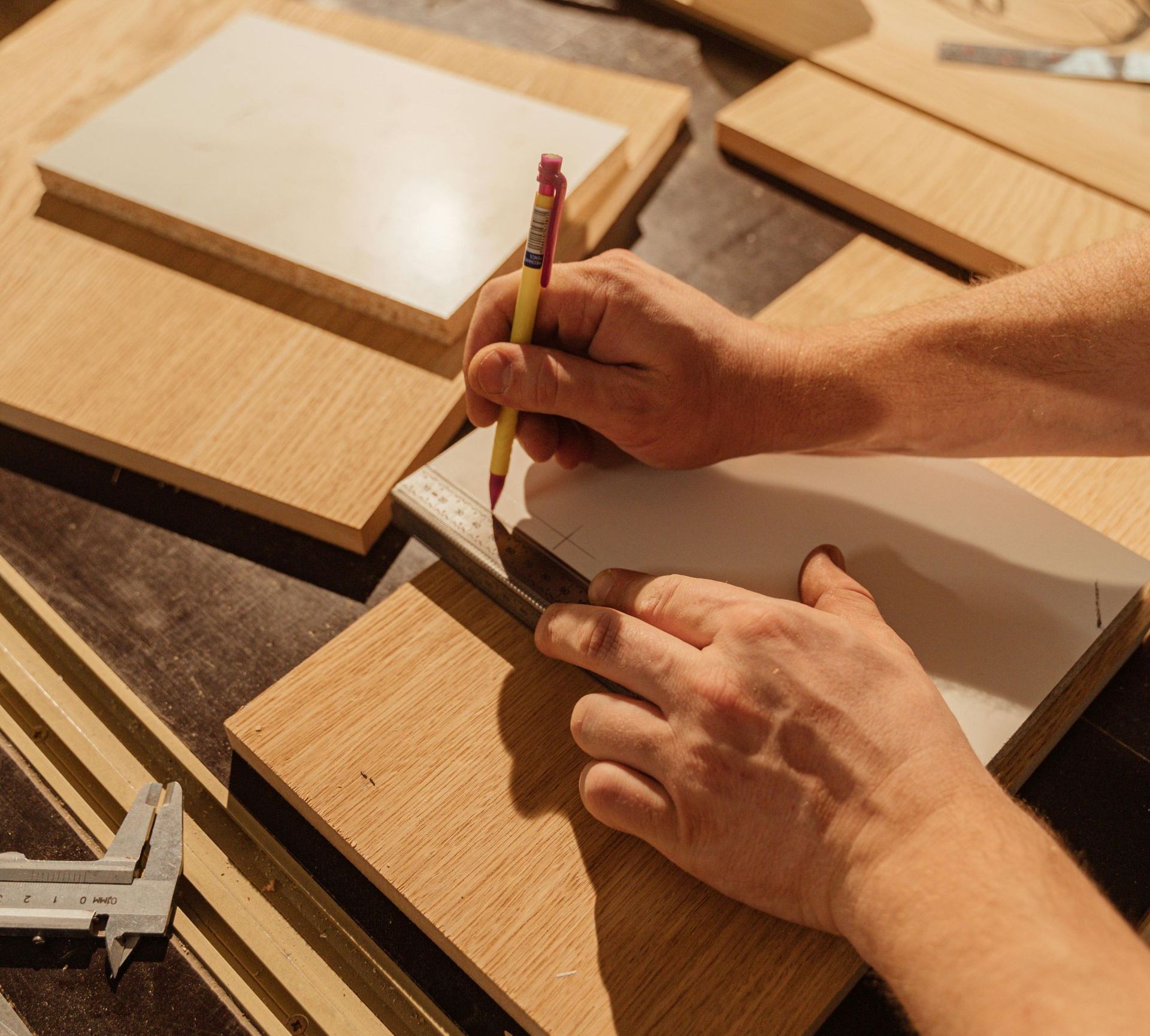 Eine Person zeichnet mit Bleistift und Lineal auf ein Stück Holz.