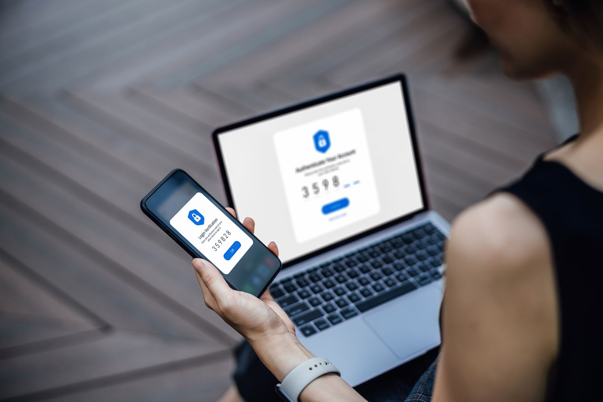 Persona che utilizza un computer portatile e uno smartphone per l'autenticazione a due fattori, con schermate di accesso corrispondenti visualizzate.
