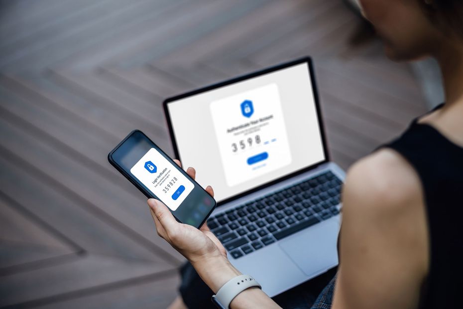 Persona che utilizza un computer portatile e uno smartphone per l'autenticazione a due fattori, con schermate di accesso corrispondenti visualizzate.
