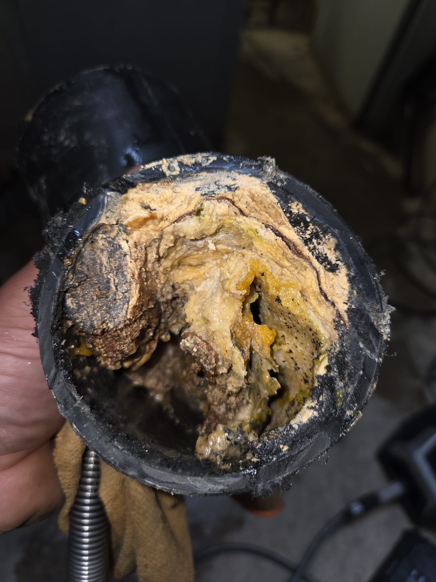 Primo piano di un tubo nero ostruito, pieno di depositi e detriti di colore giallo-marrone.