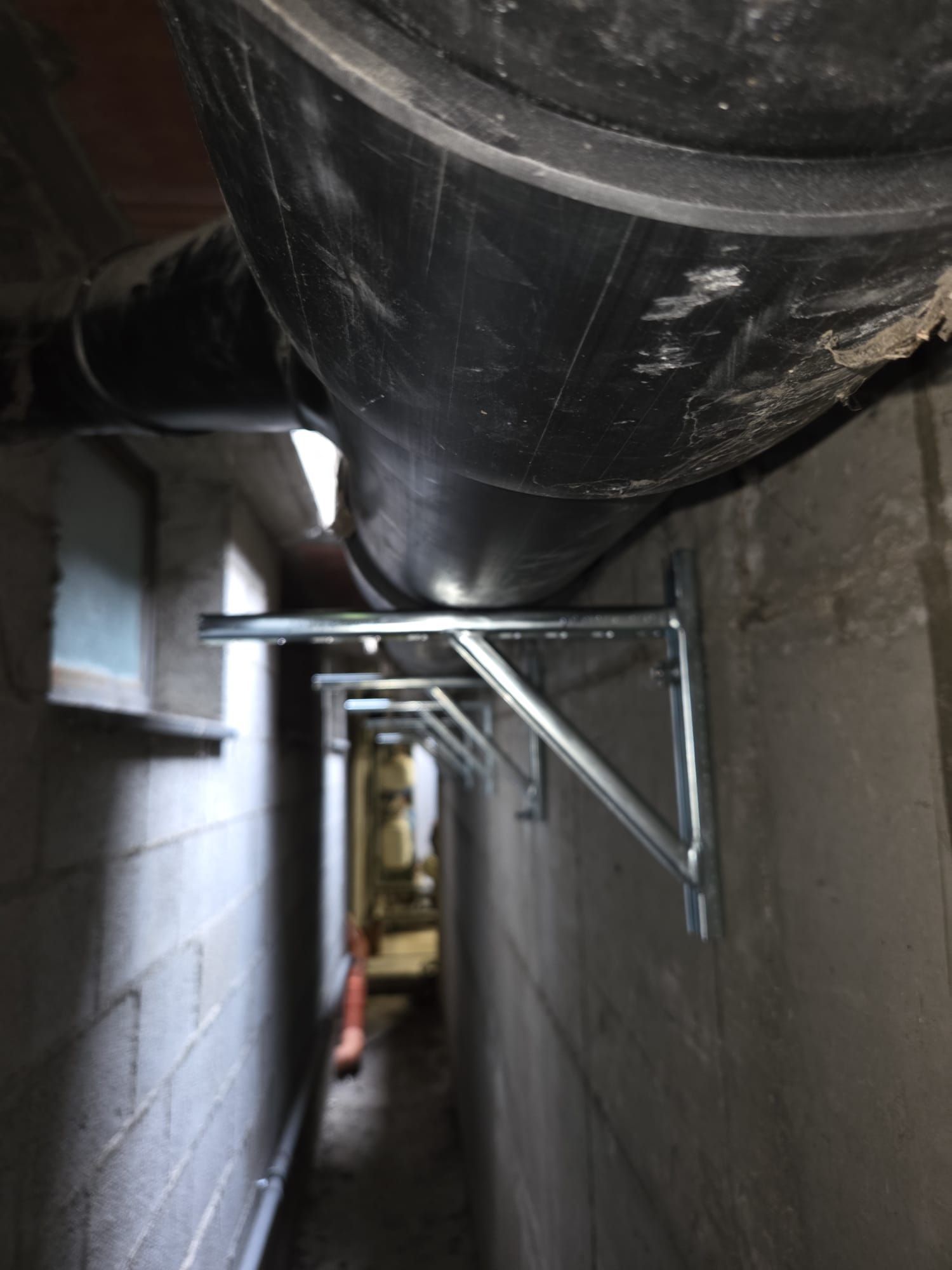 Un grosso tubo nero in uno stretto corridoio, sorretto da una staffa metallica vicino al soffitto.