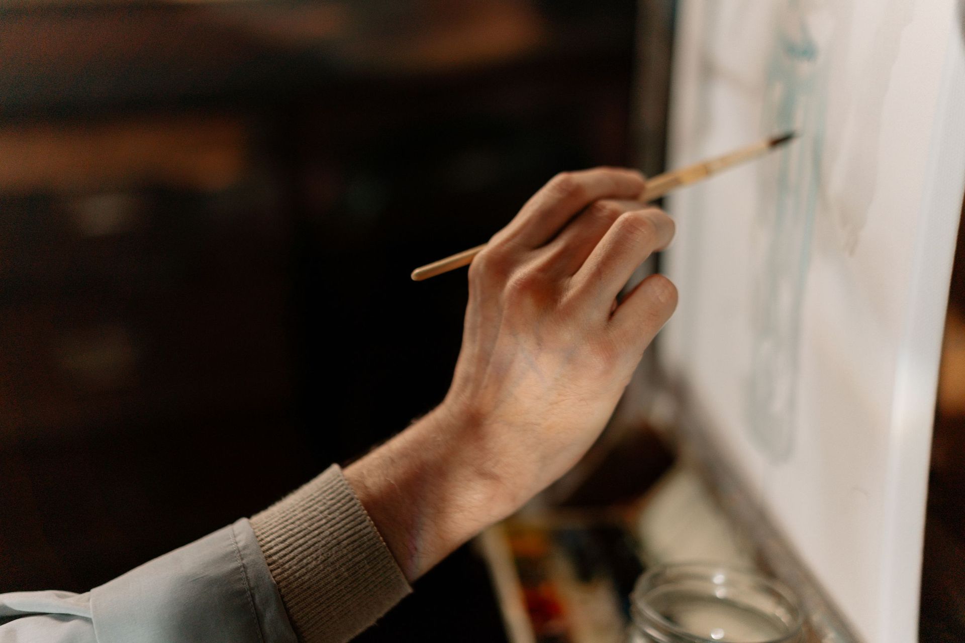 A hand holding a paintbrush in warm, low studio light