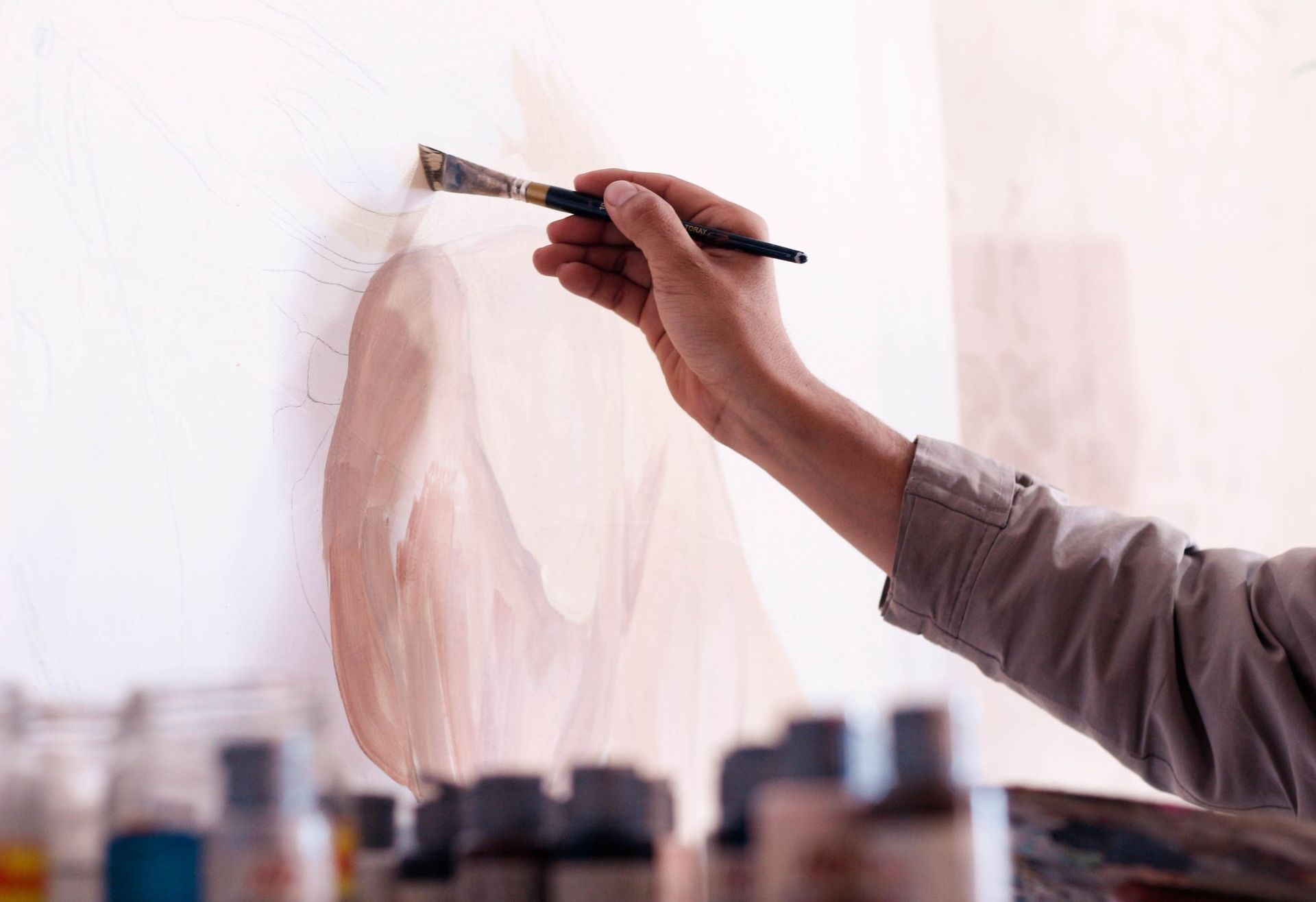 A hand brushing a soft blush wash across a white canvas