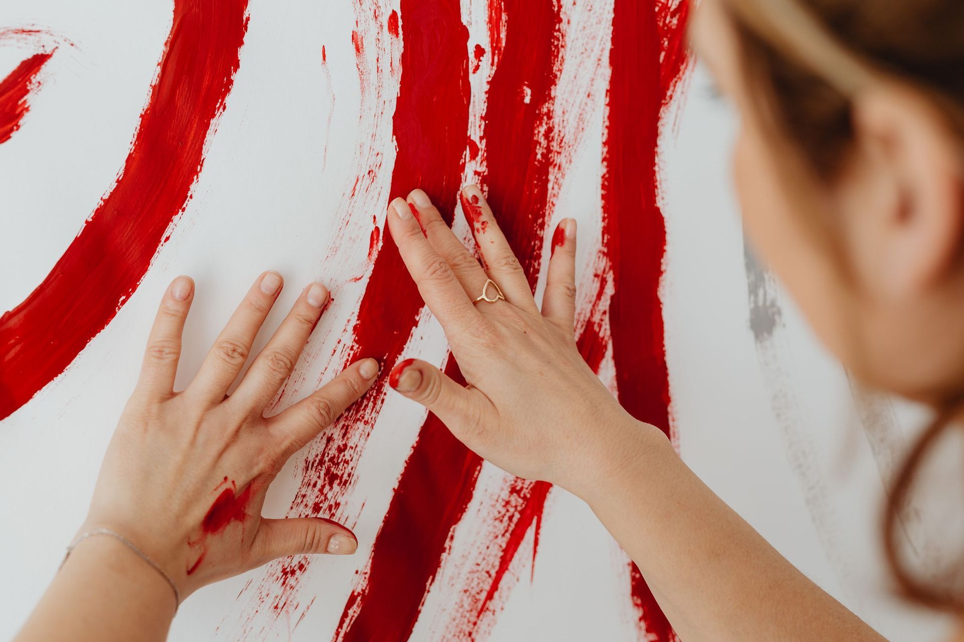 Two open palms pressed into wide red brush strokes on a white canvas