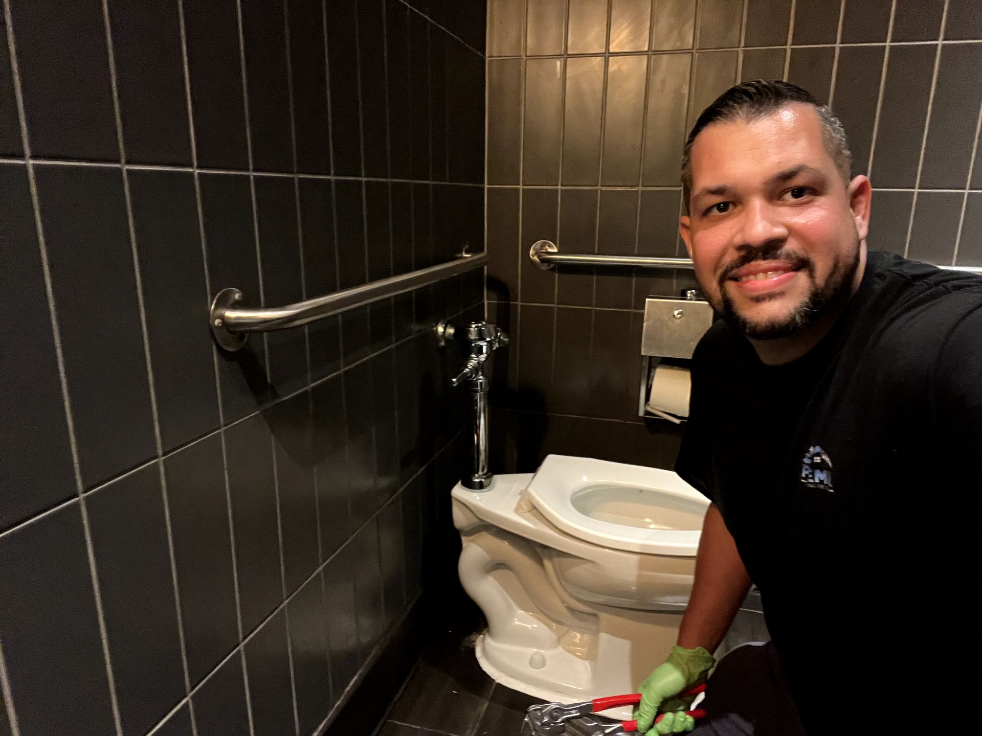 A man is cleaning a toilet in a public restroom.