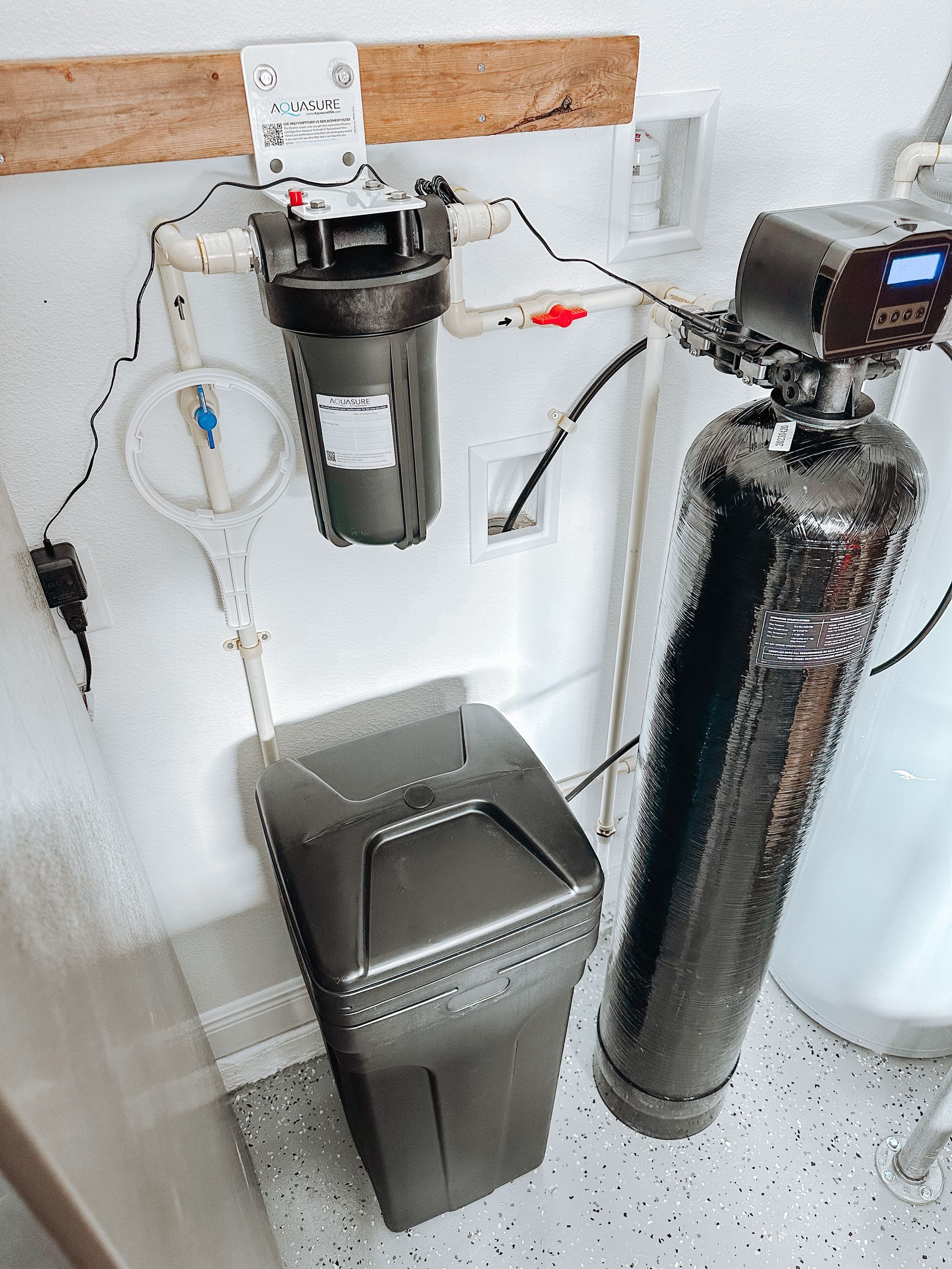 A water filter is sitting next to a trash can in a bathroom.