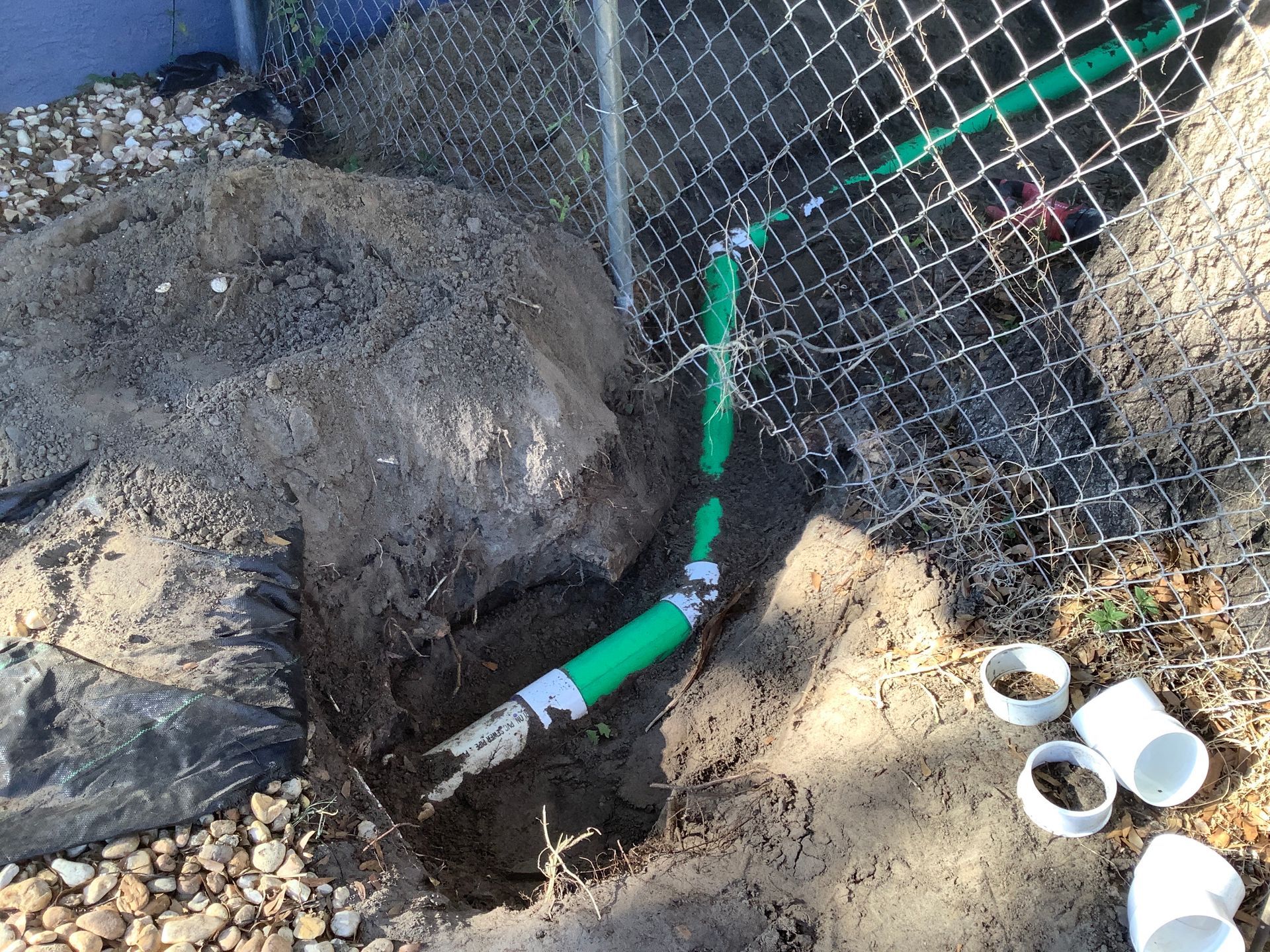 A green pipe is laying in the dirt next to a chain link fence.