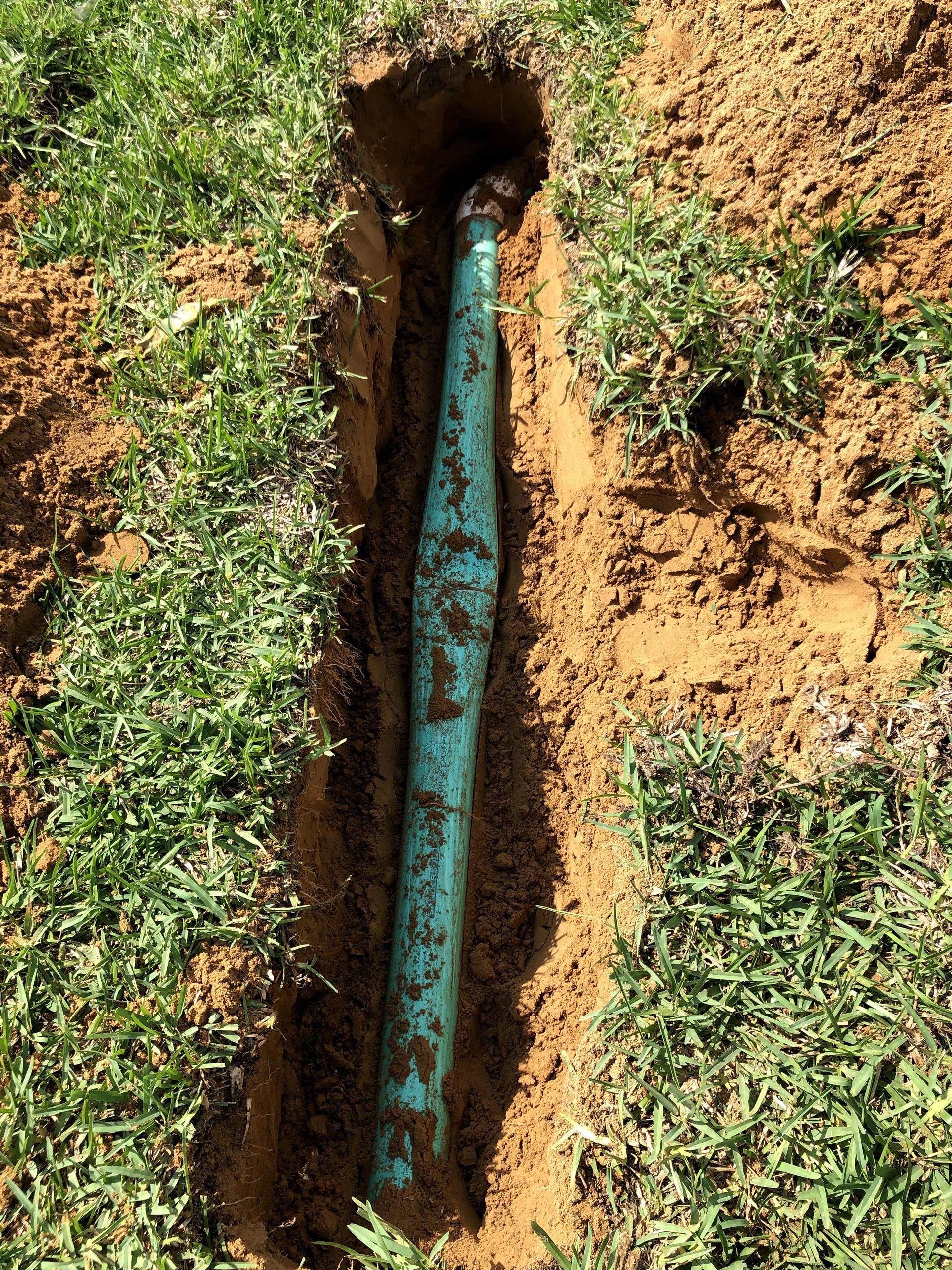 A green pipe is sticking out of a hole in the ground.