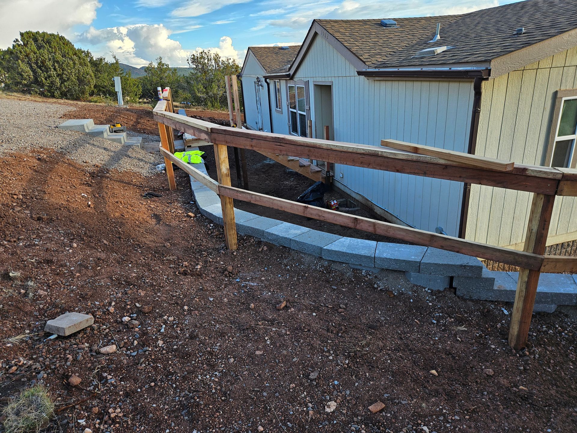 Two workers leveling fresh gravel beside a house in a wooded yard