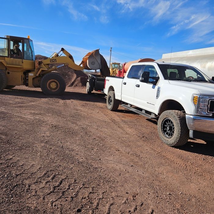 White pickup truck beside a yellow bulldozer at a dirt worksite under a blue sky