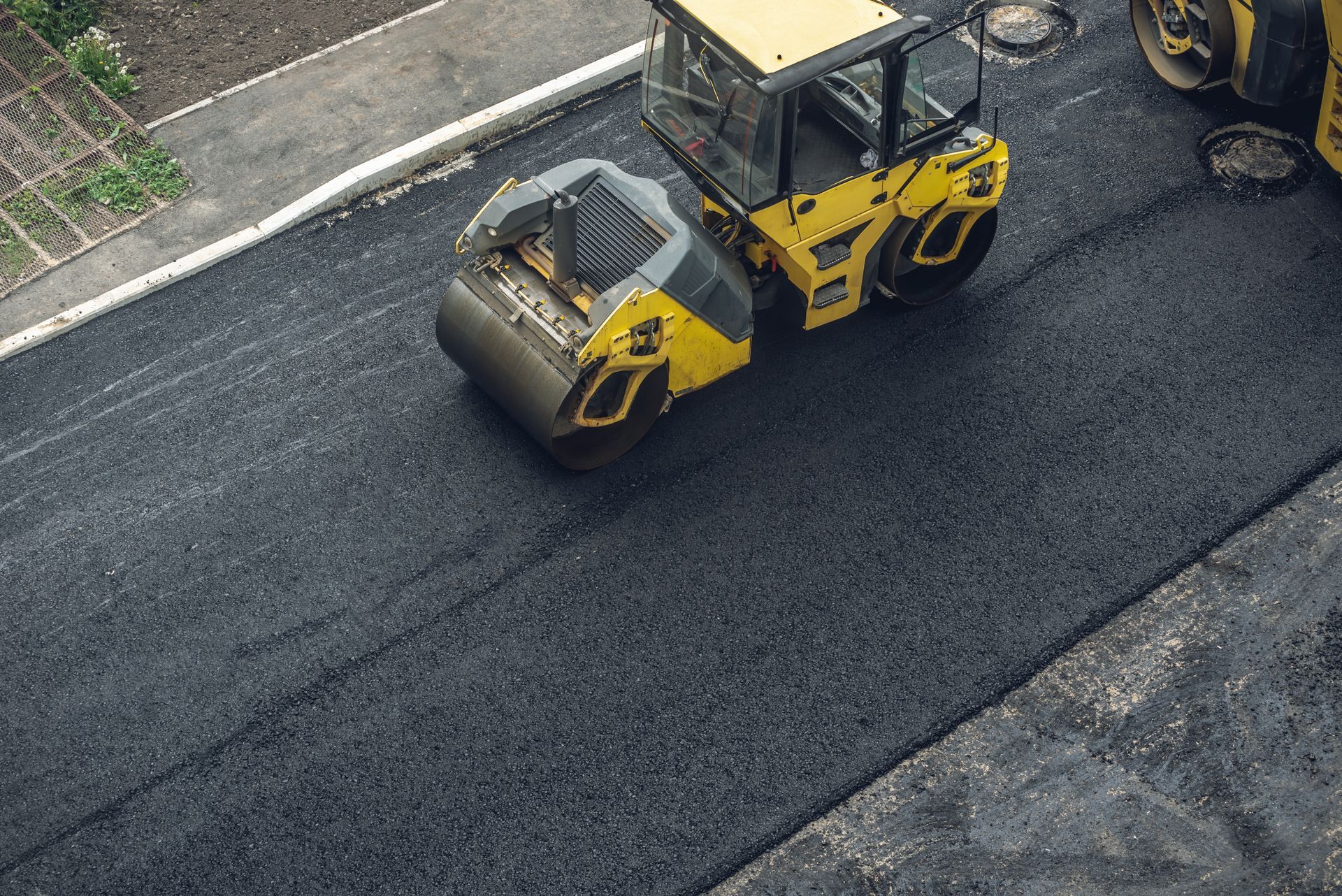 Yellow road roller paving a dark asphalt street beside a curb