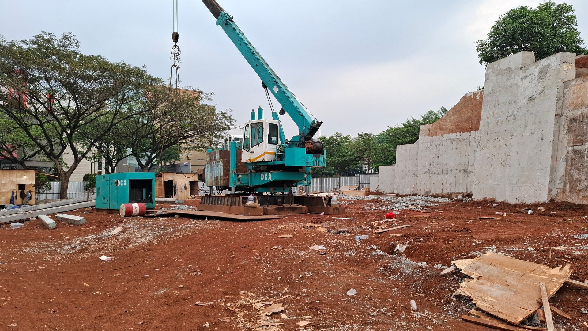 Construction site with crane lifting near a partially demolished brick building on a red dirt lot