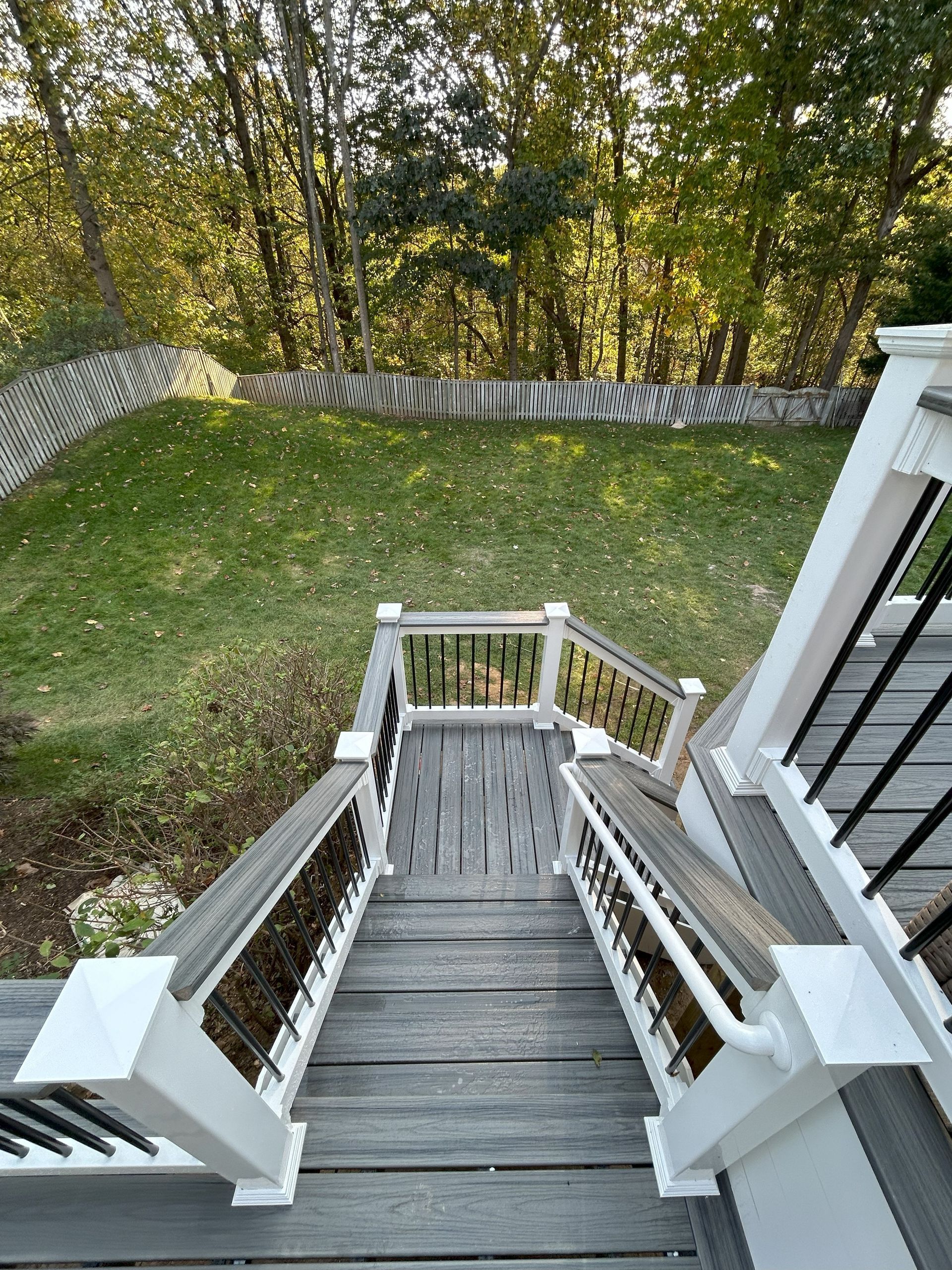 Wooden deck stairs leading down to a grassy yard, surrounded by trees.