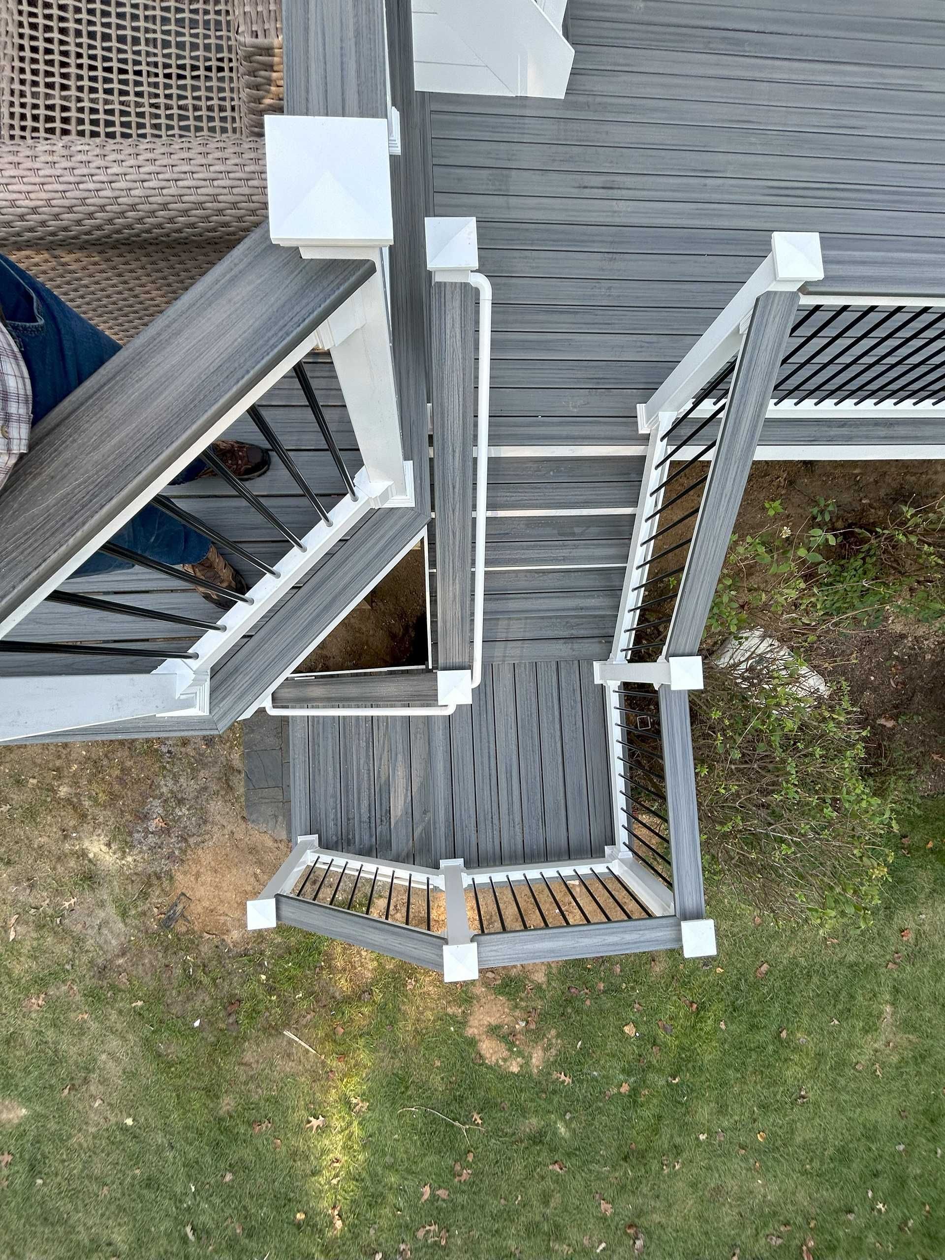 Overhead view of a gray and white deck with black railings on green grass.