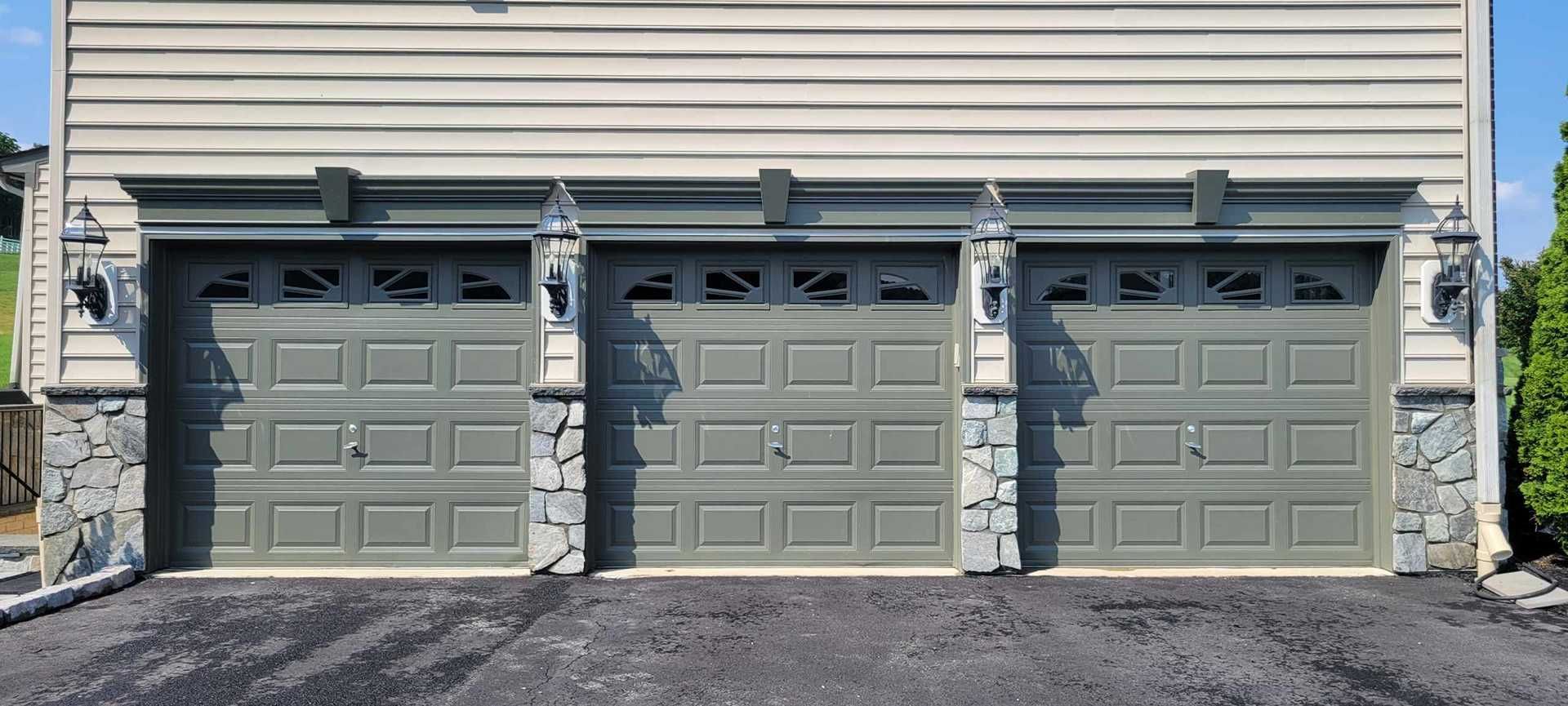Three-door gray garage with stone accents, lights, and a driveway.