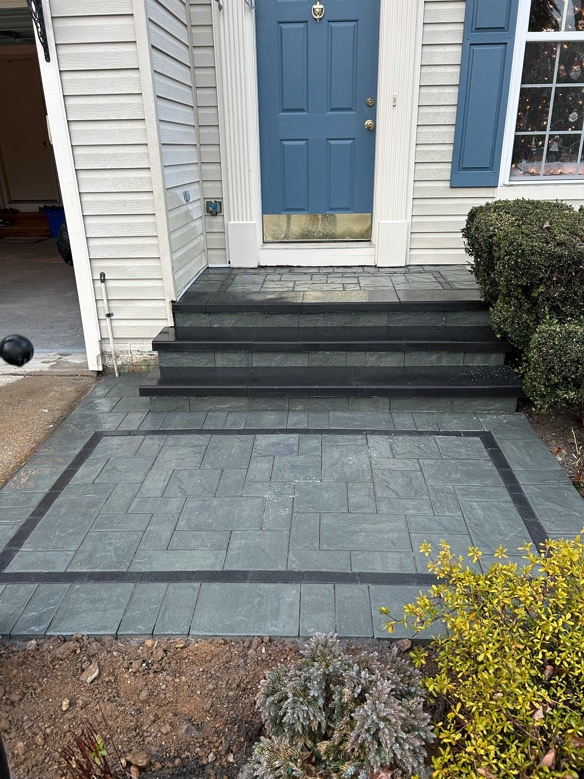 Gray paved walkway and steps leading to a blue door. Black border detail. Small shrubs on each side.