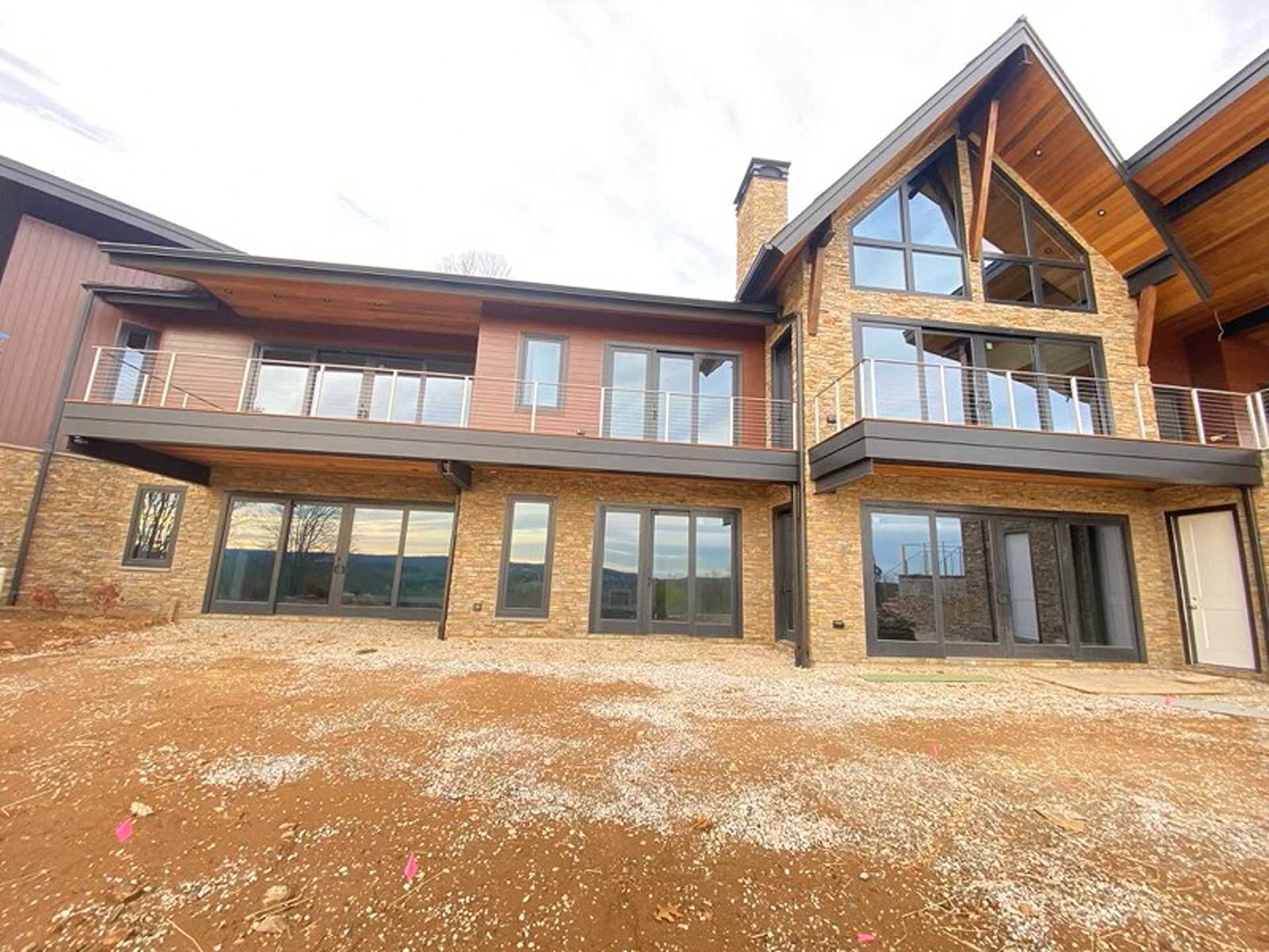 Two-story luxury house with brick and wood siding, large windows, and an unfinished yard.