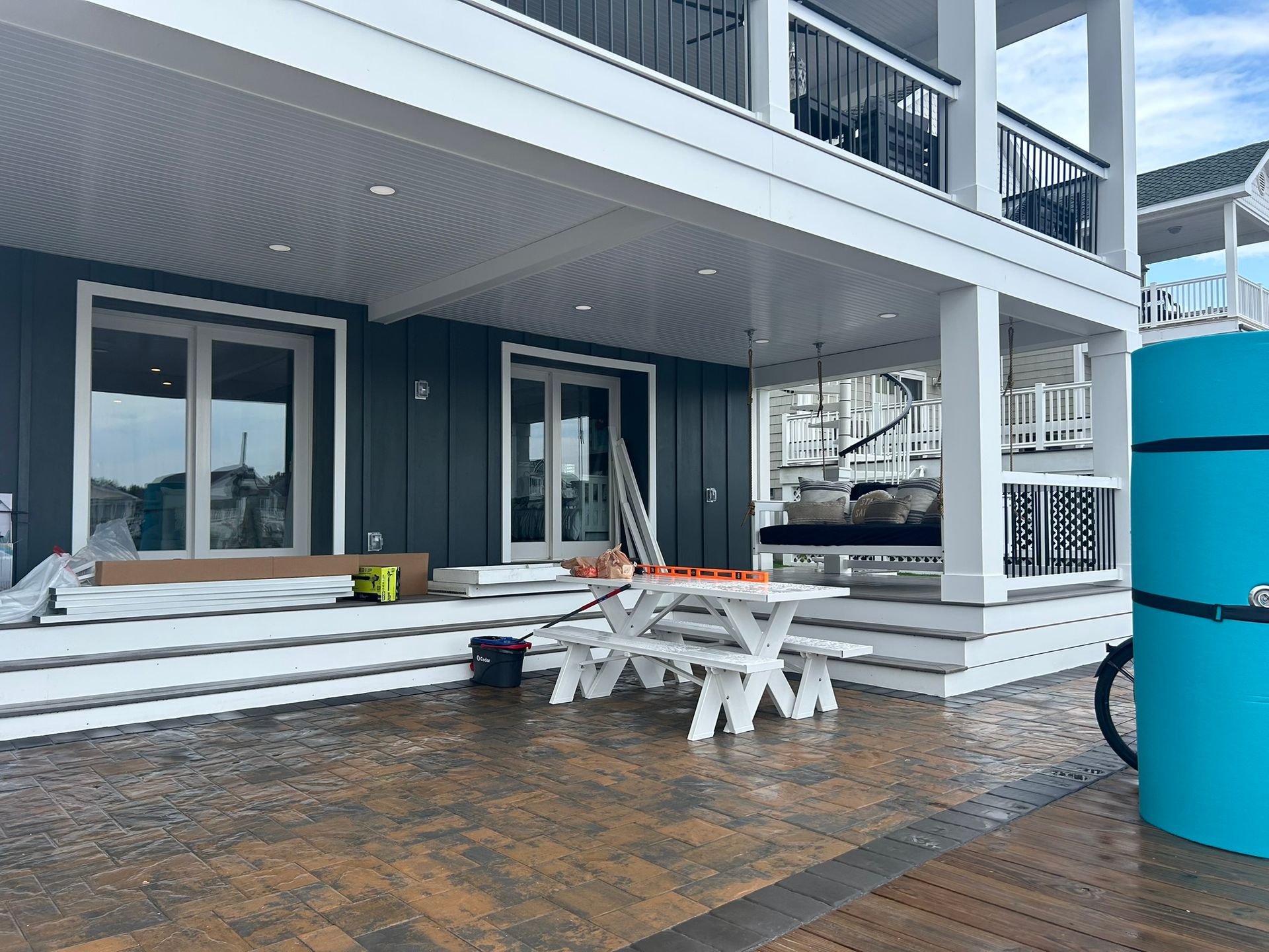 Exterior of a house with a porch and picnic table. Gray siding, white trim. Blue water tank on the right.