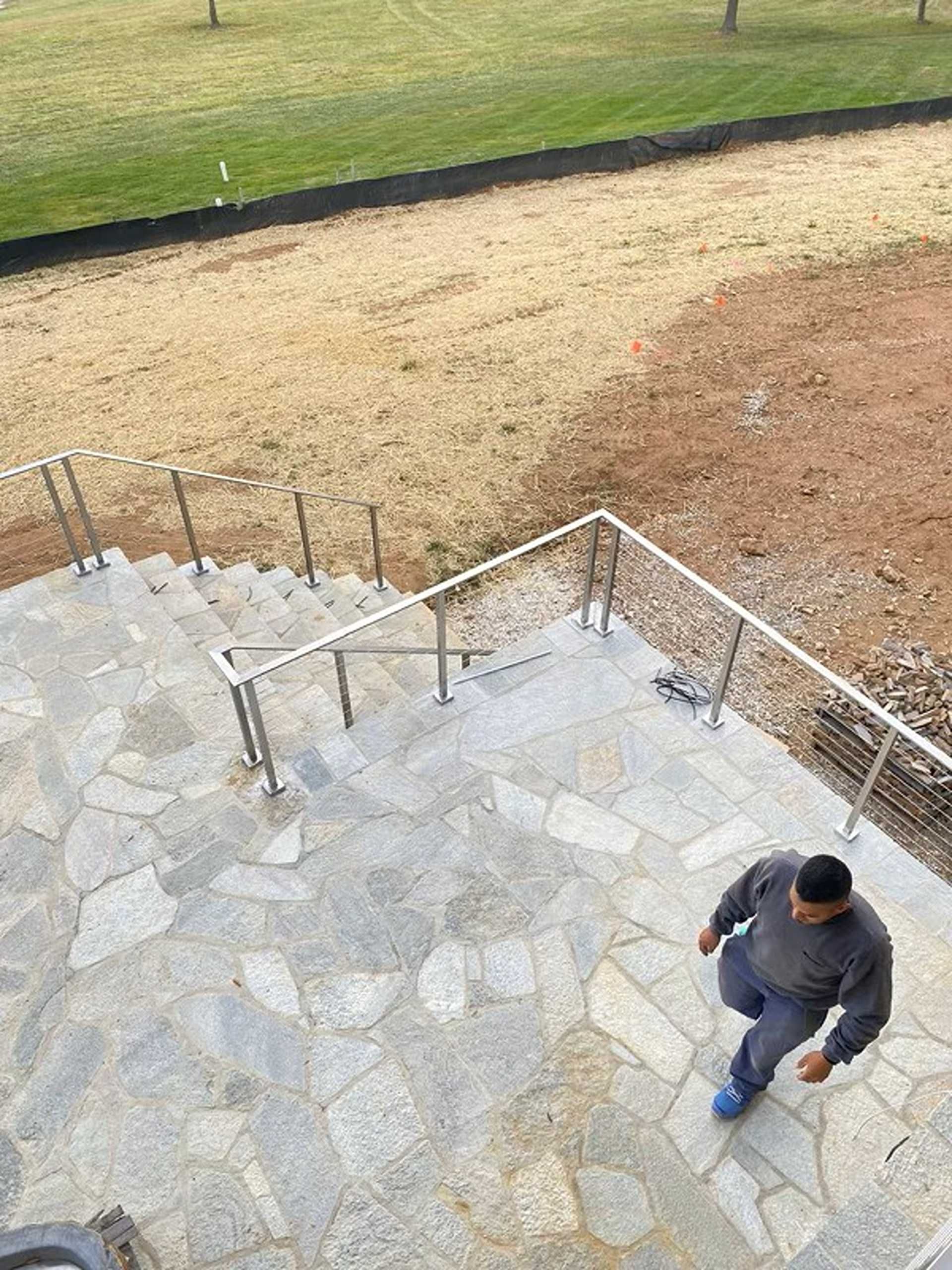 Person walking down stone stairs with metal handrails; grassy area in background.