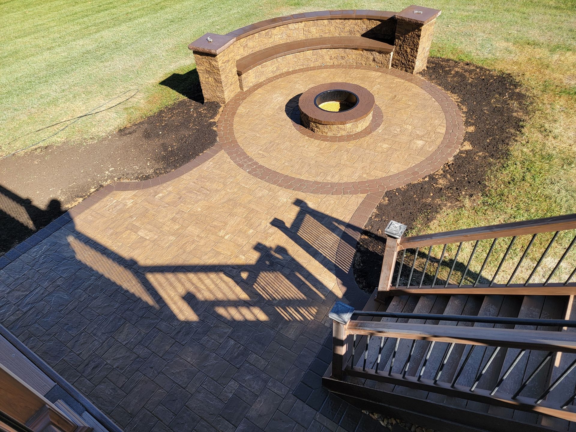 Stone patio with fire pit and built-in seating. Pathway leads from wooden stairs down to the area.