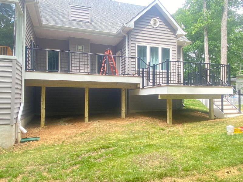Exterior view of a house with a newly constructed deck featuring black railings and wooden supports, set on a grassy lawn.
